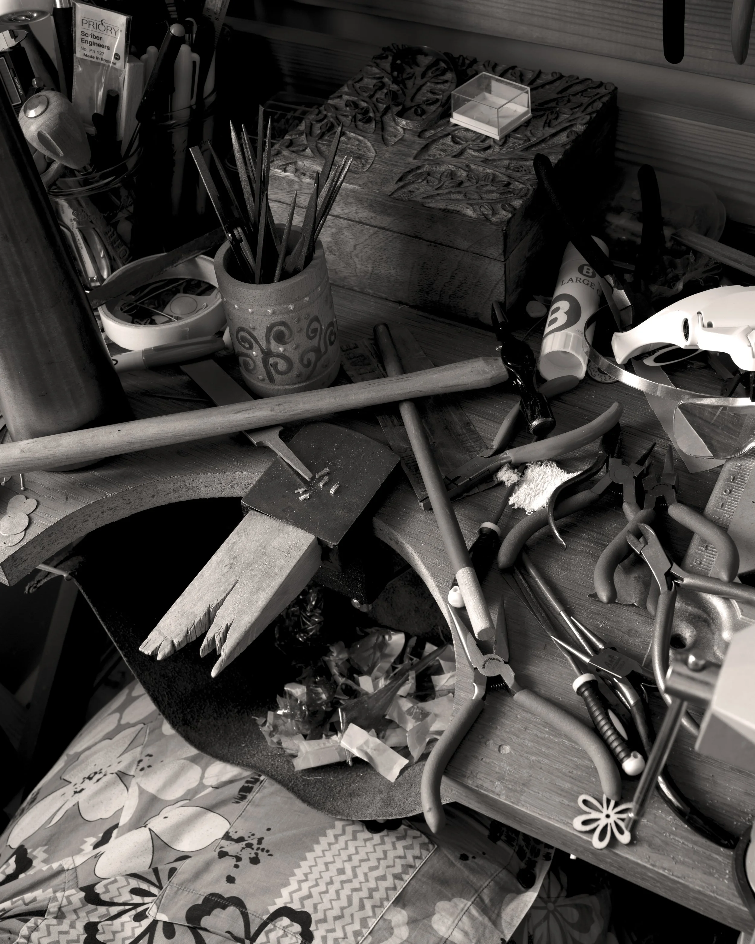 A cluttered workspace with various tools and materials scattered across a wooden table, including pliers, a hammer, a plastic bottle, a helmet, and a carved wooden piece.