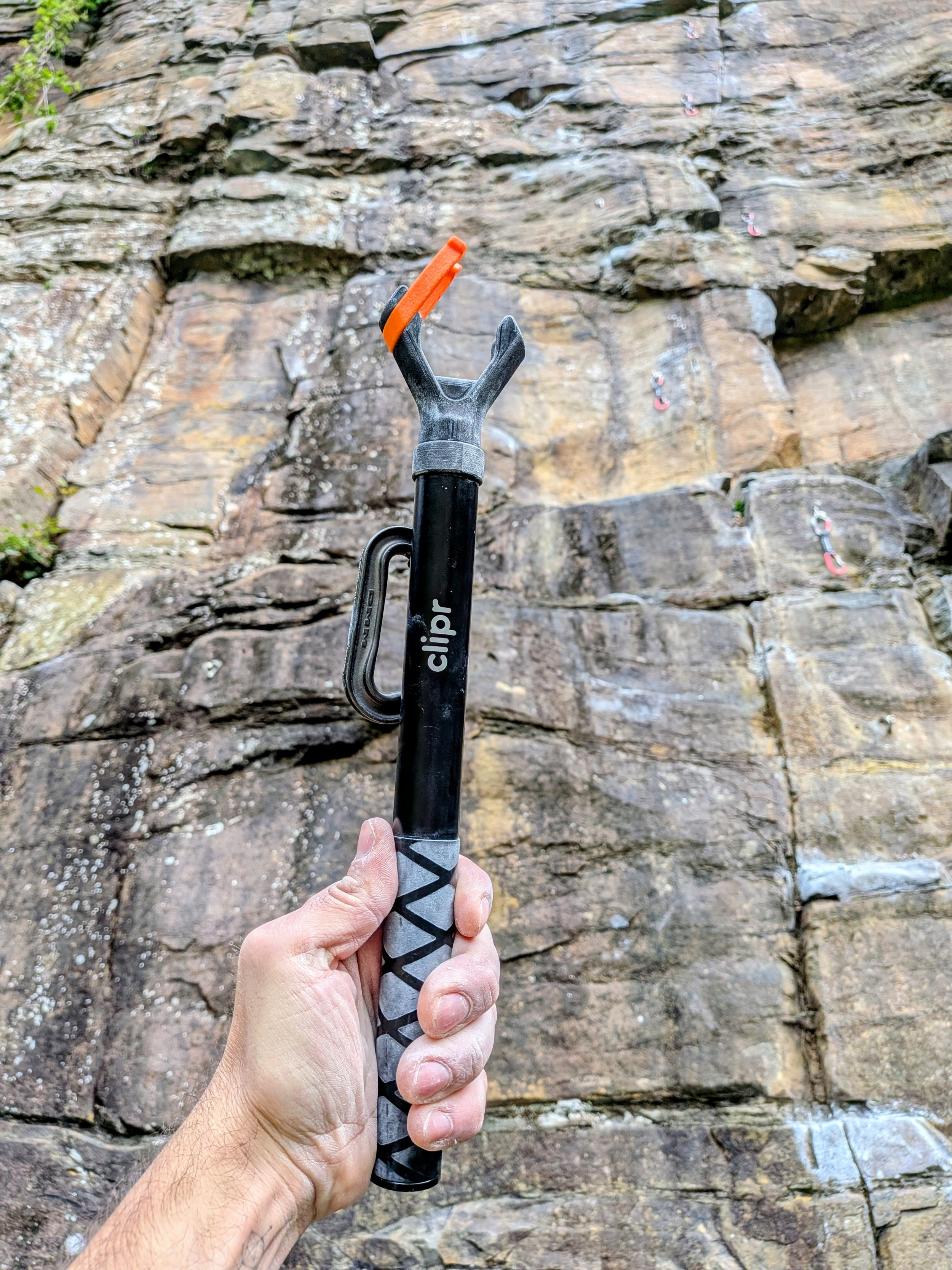 Person holding a clipr rock climbing clip stick in front of a rock wall with multiple chalked climbing holds.