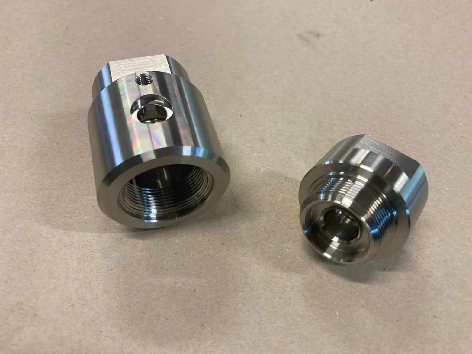 Due componenti meccanici in metallo con filettature, uno più grande dell'altro, dal design cilindrico e superfici lisce e riflettenti.
