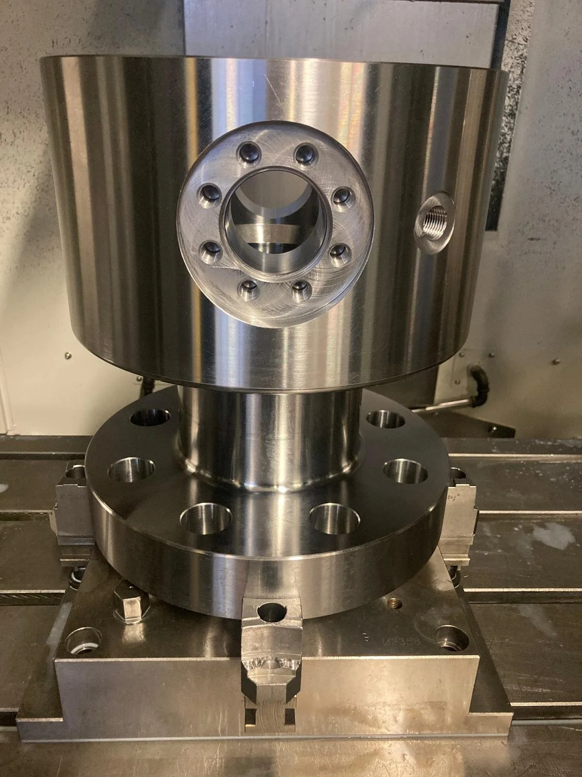 Componenti meccanici in metallo lucido, parte di un macchinario industriale, con fori e raccordi, montati su una piattaforma.