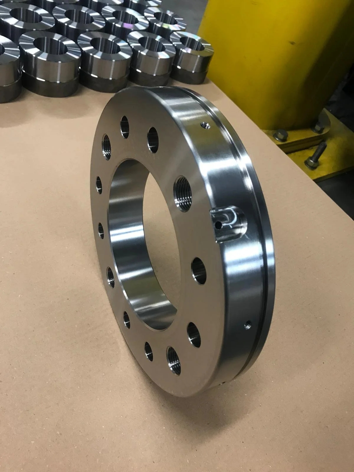 Anello metallico grande con vari fori e filettature, posizione a riposo su una superficie di lavoro in un ambiente di fabbrica.