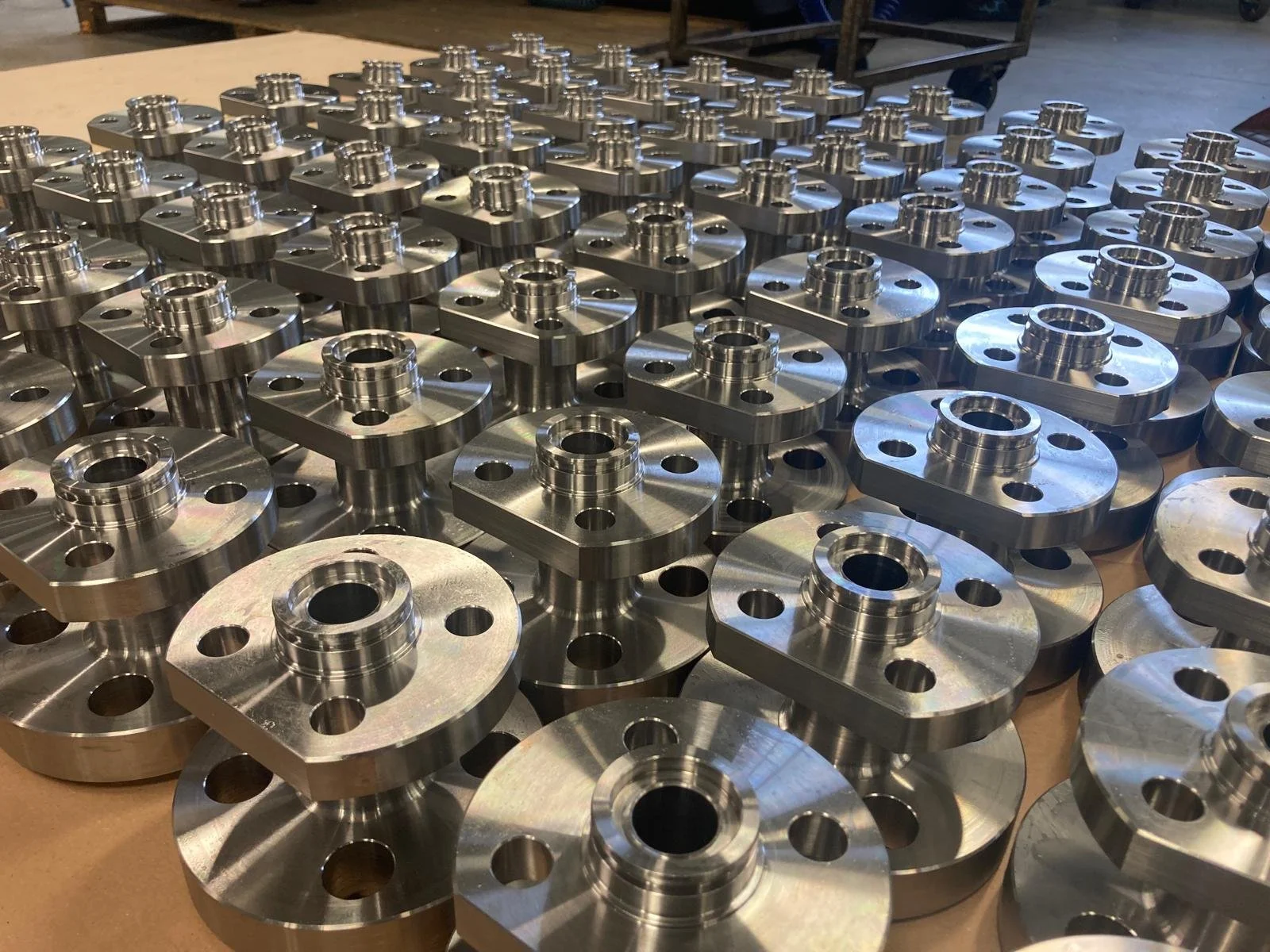 Numerosi componenti metallici cilindrici e quadrati su banco di lavoro in un'officina.