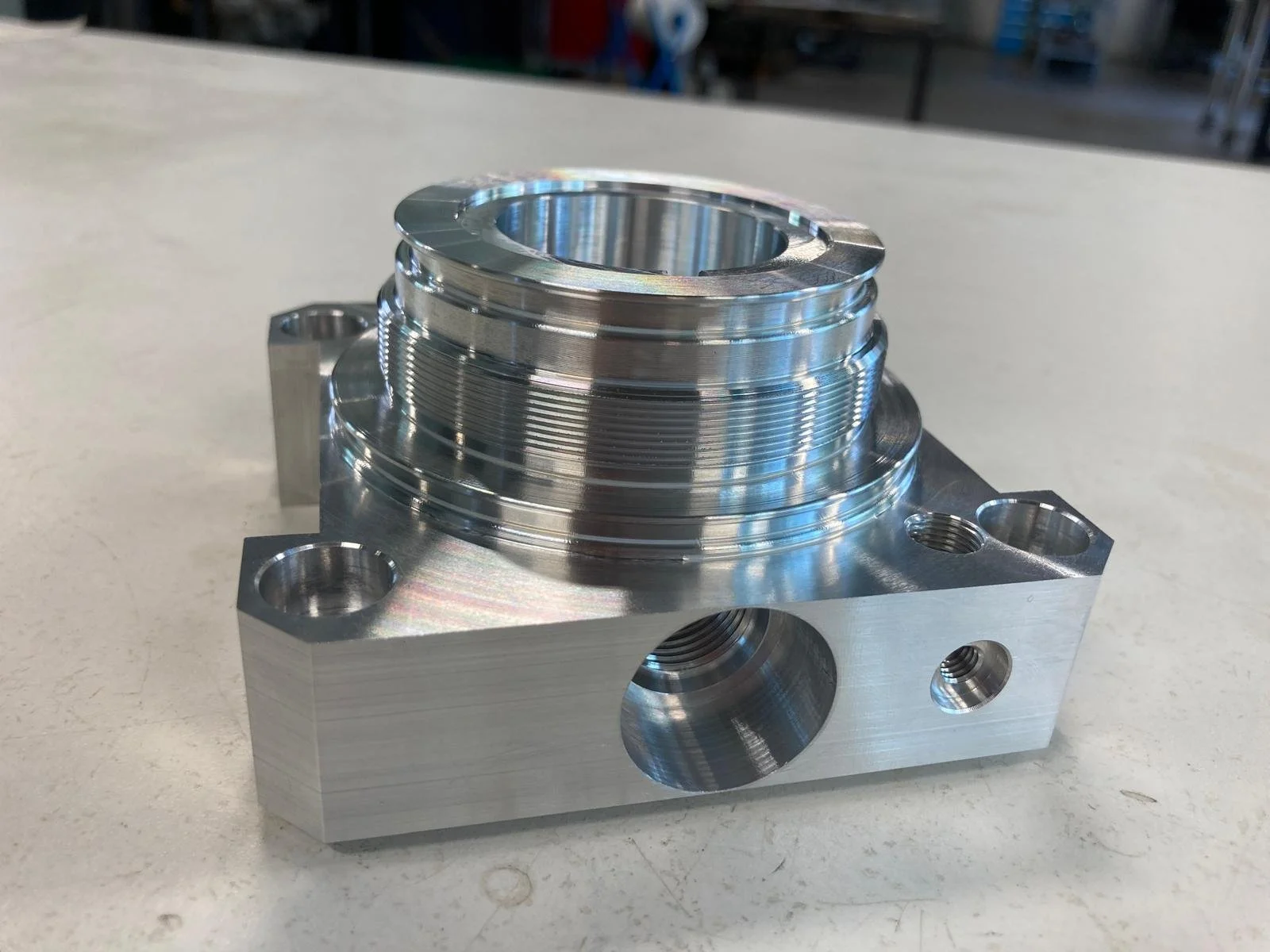 Particolare meccanico in metallo lucido con fori e raccordi, probabilmente una componente di macchina o ingranaggio.