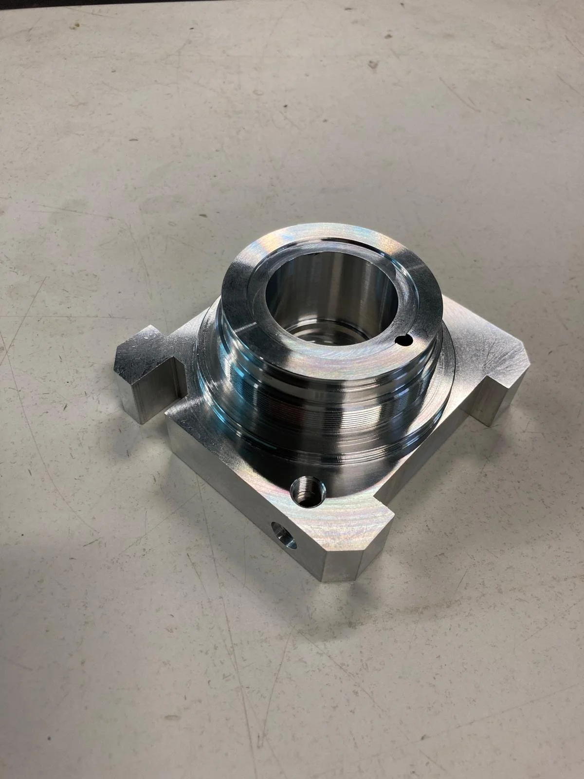 Componente meccanico in metallo lucido, con forma cilindrica e pincolo foro, posizionato su una superficie chiara.