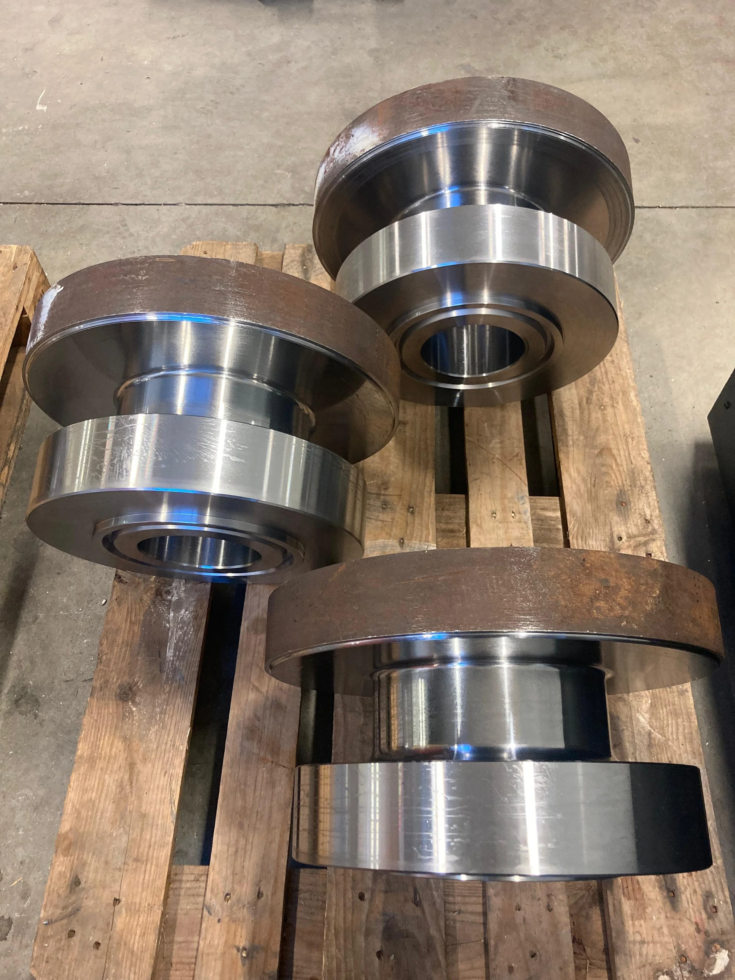 Due grandi rulli metallici lisci e lucidi sono poggiati su un pallet di legno.