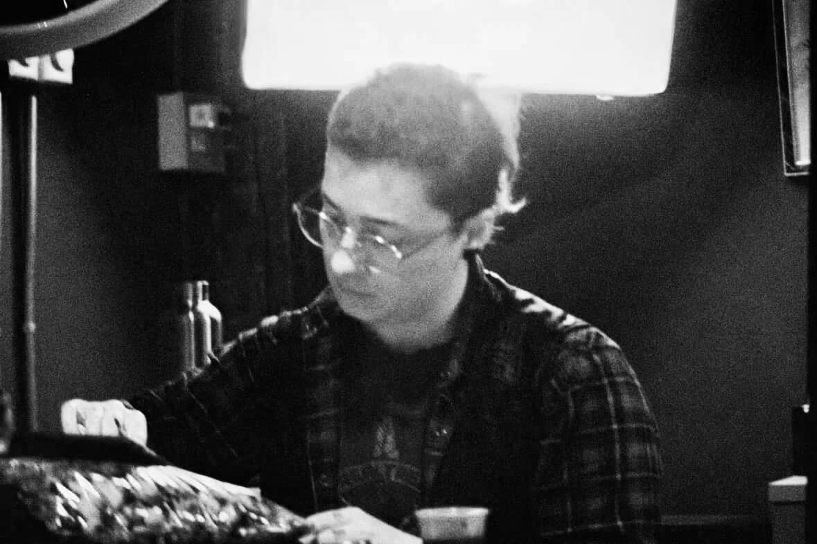 A person with short hair and glasses wearing a plaid shirt, looking down while drawing.