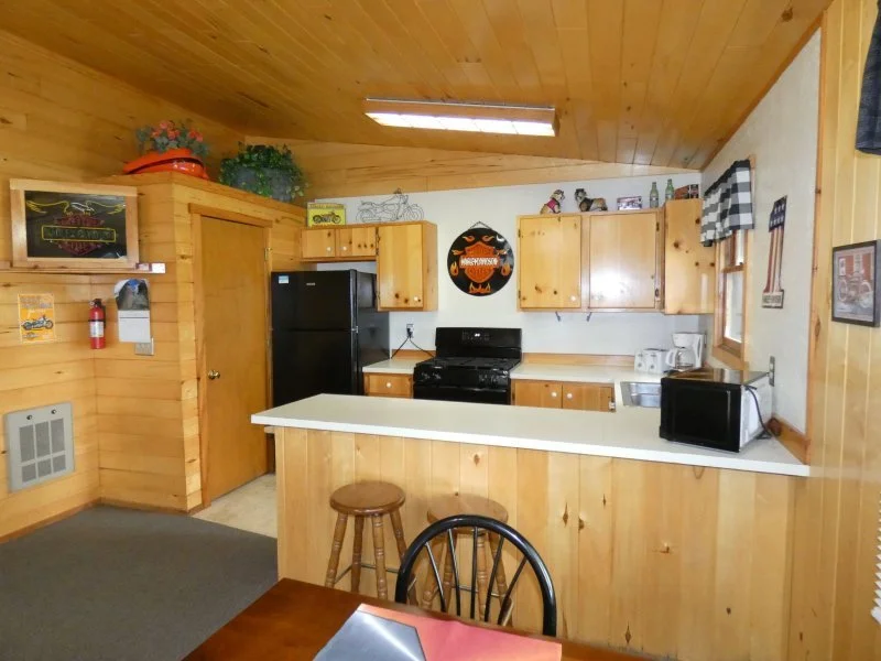 Kitchen with wooden cabinets and walls, black refrigerator, black stove, microwave, coffee maker, and wall-mounted Halloween decoration