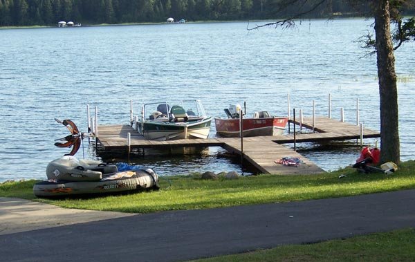 Dock with two boats, a jet ski, and fishing gear on grassy shoreline beside a lake.
