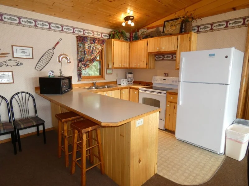 Cozy kitchen with wooden cabinets, white appliances, and a breakfast bar with two stools.