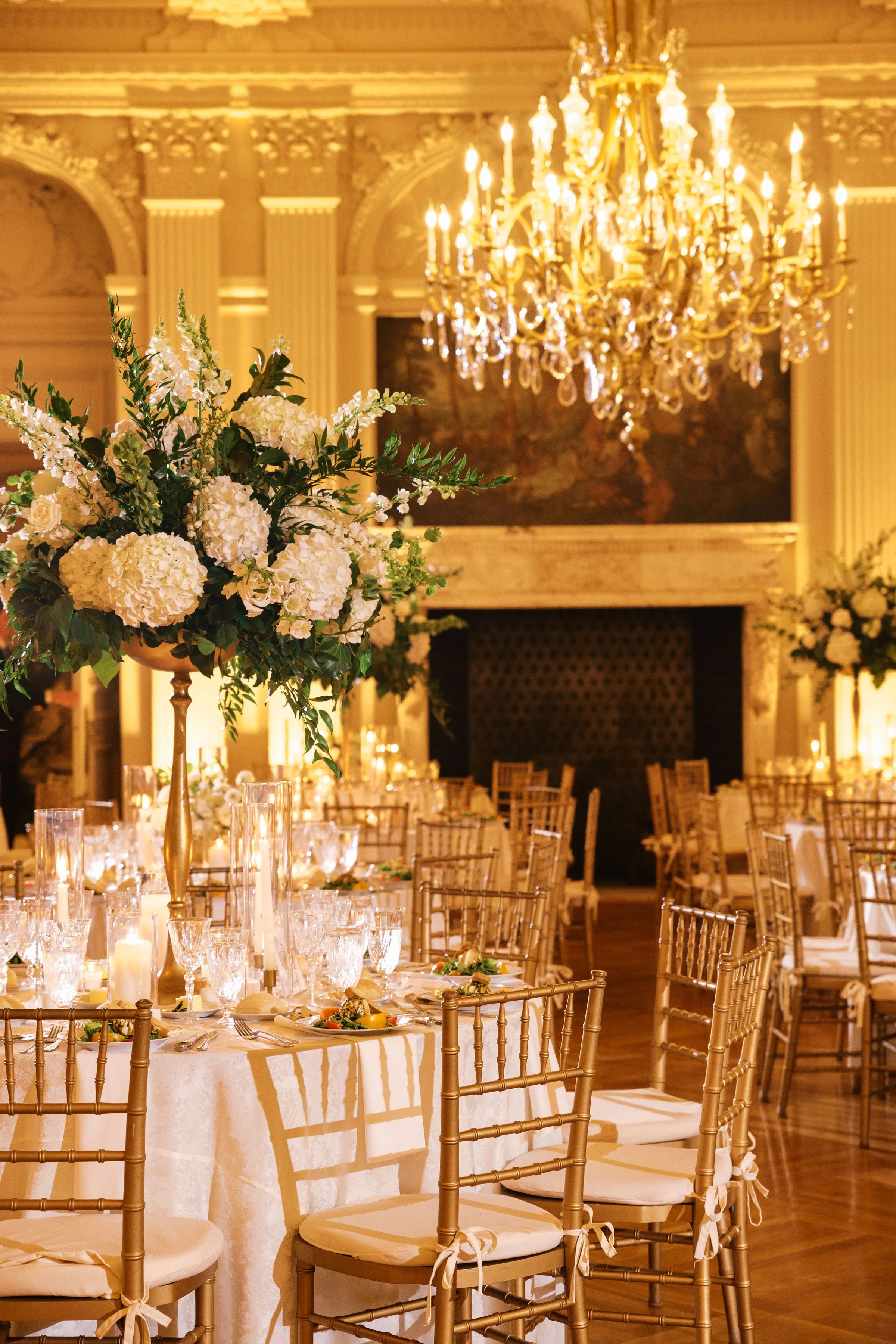 Elegant banquet hall with a large floral centerpiece, gold chairs, and a grand chandelier.