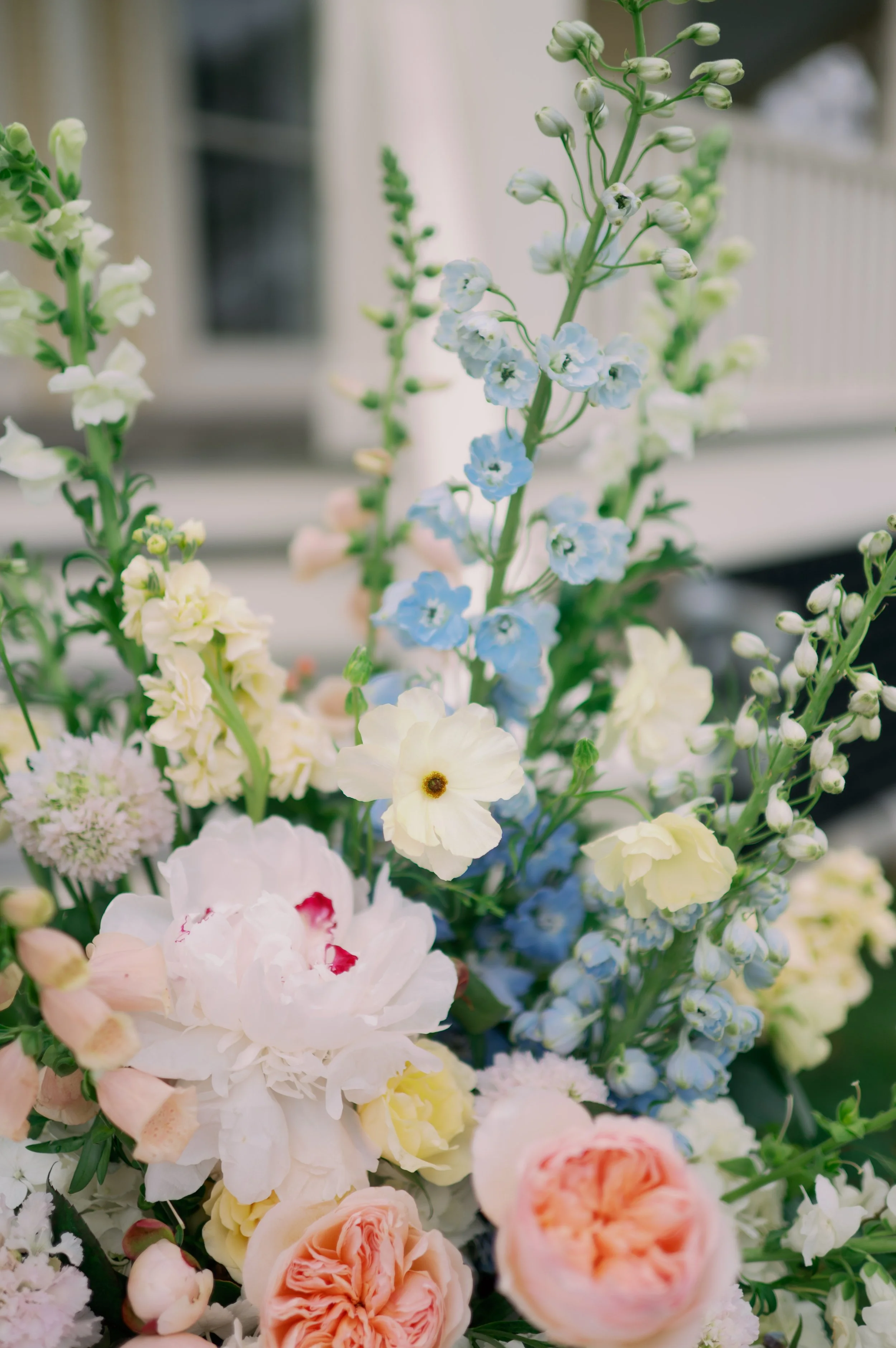 A colorful bouquet of various flowers including white, pink, peach, and blue blossoms with green stems and leaves.