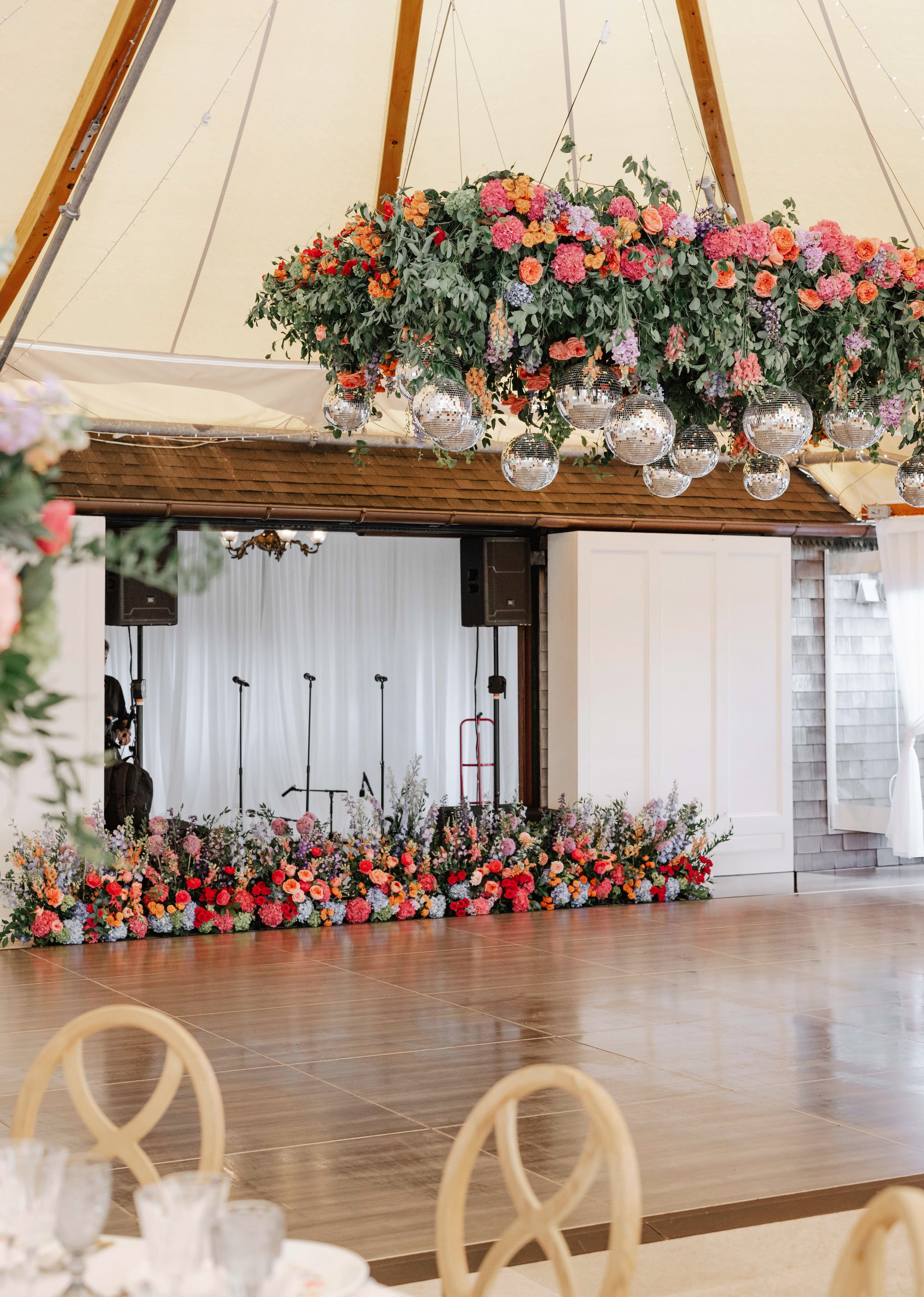 Floral decoration with hanging disco balls above a stage at an event venue. The stage is surrounded by a colorful flower arrangement.