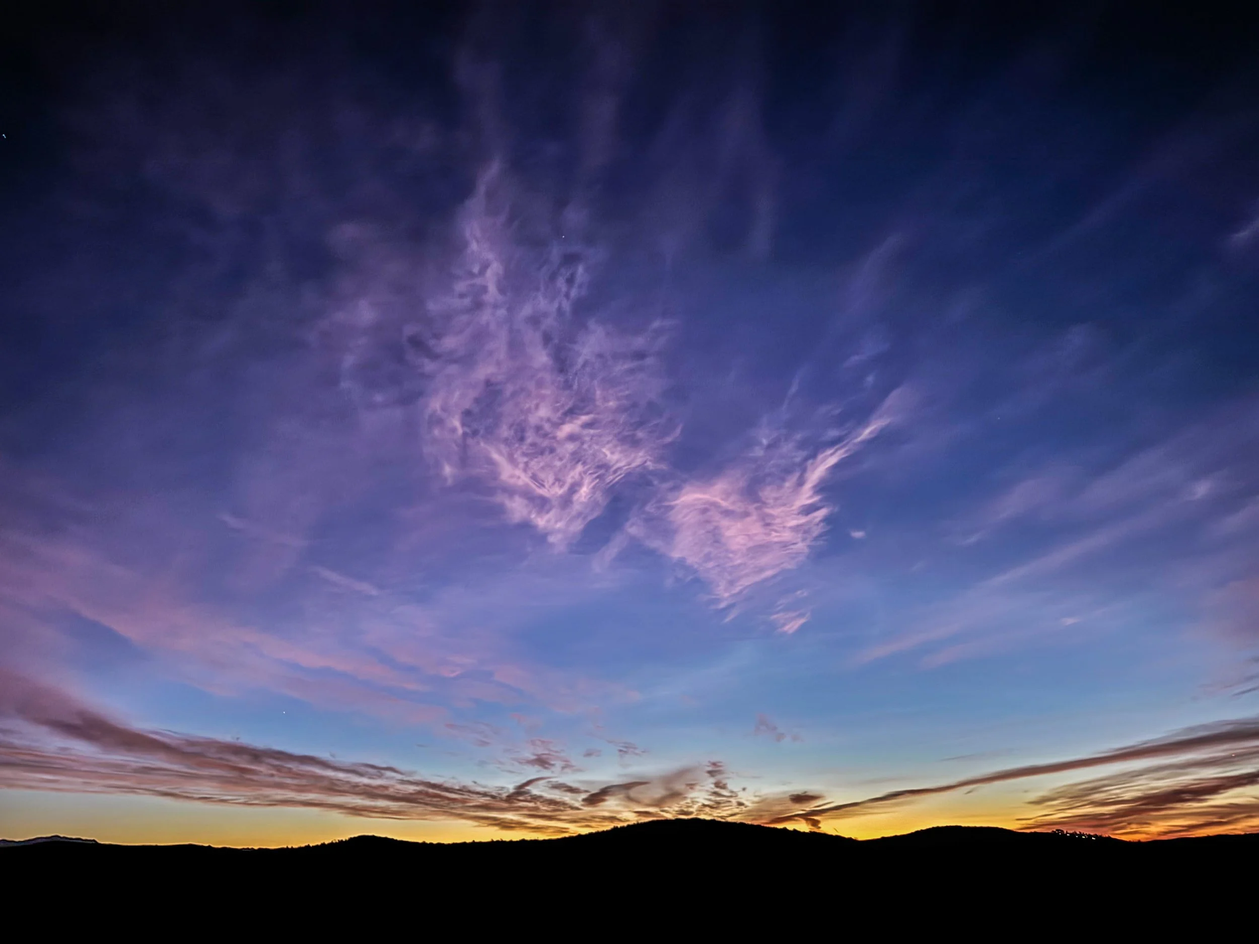 Colorful sky at sunset with purple, pink, and orange clouds above silhouetted hills.