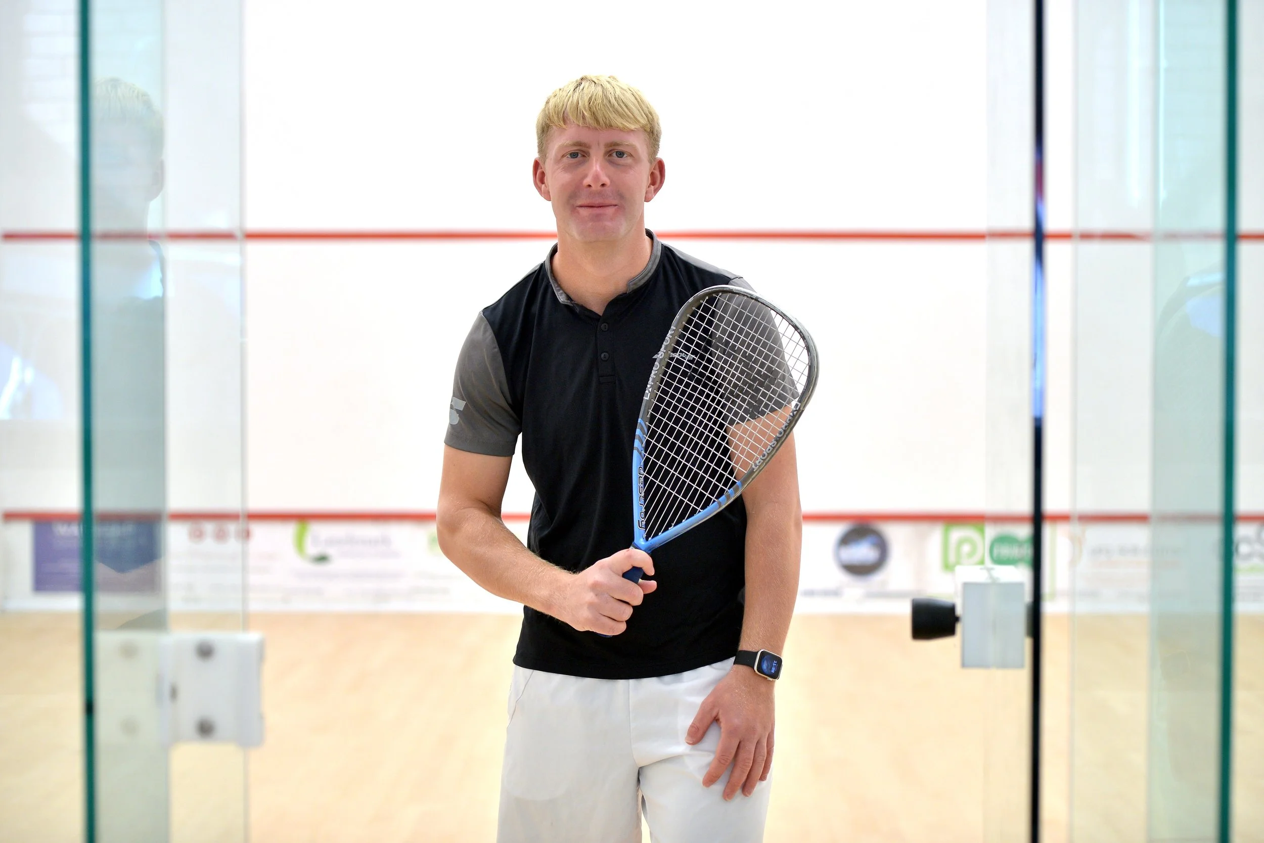 A man holding a squash racquet inside a squash court.