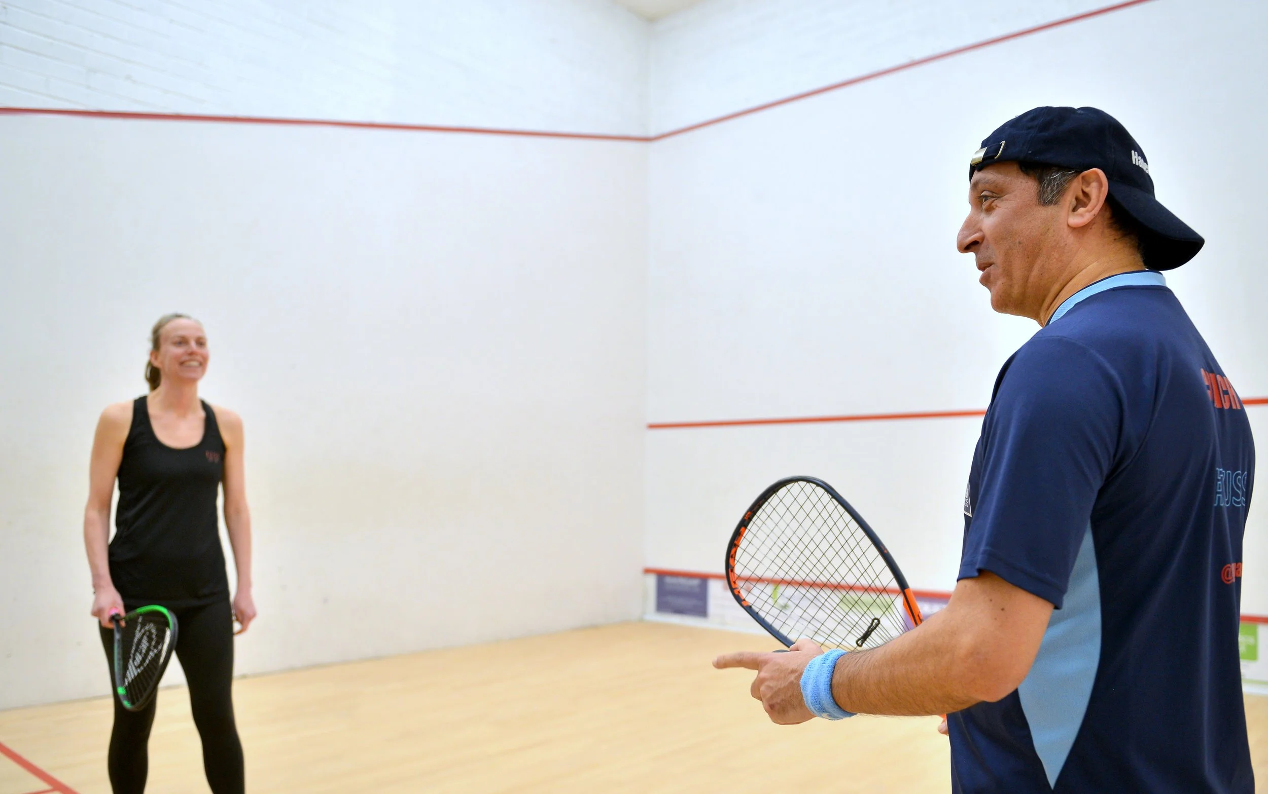 A woman playing squash in an indoor court, preparing to hit the ball with her racket.
