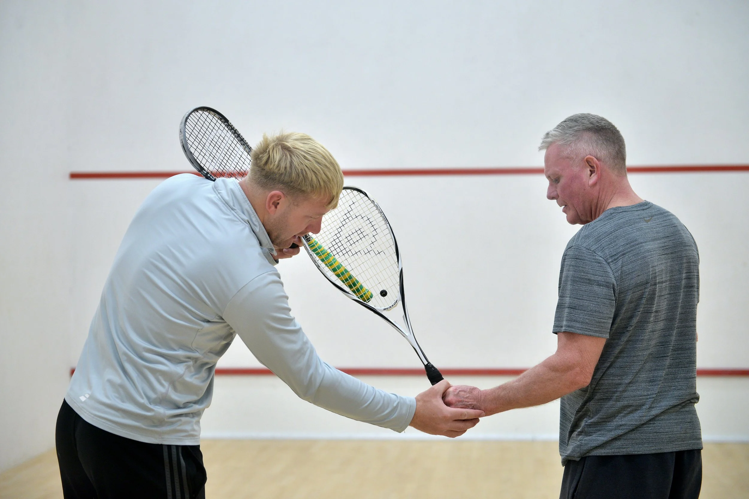 Two men playing squash on an indoor court, one holding a squash racket and the other holding his hand.