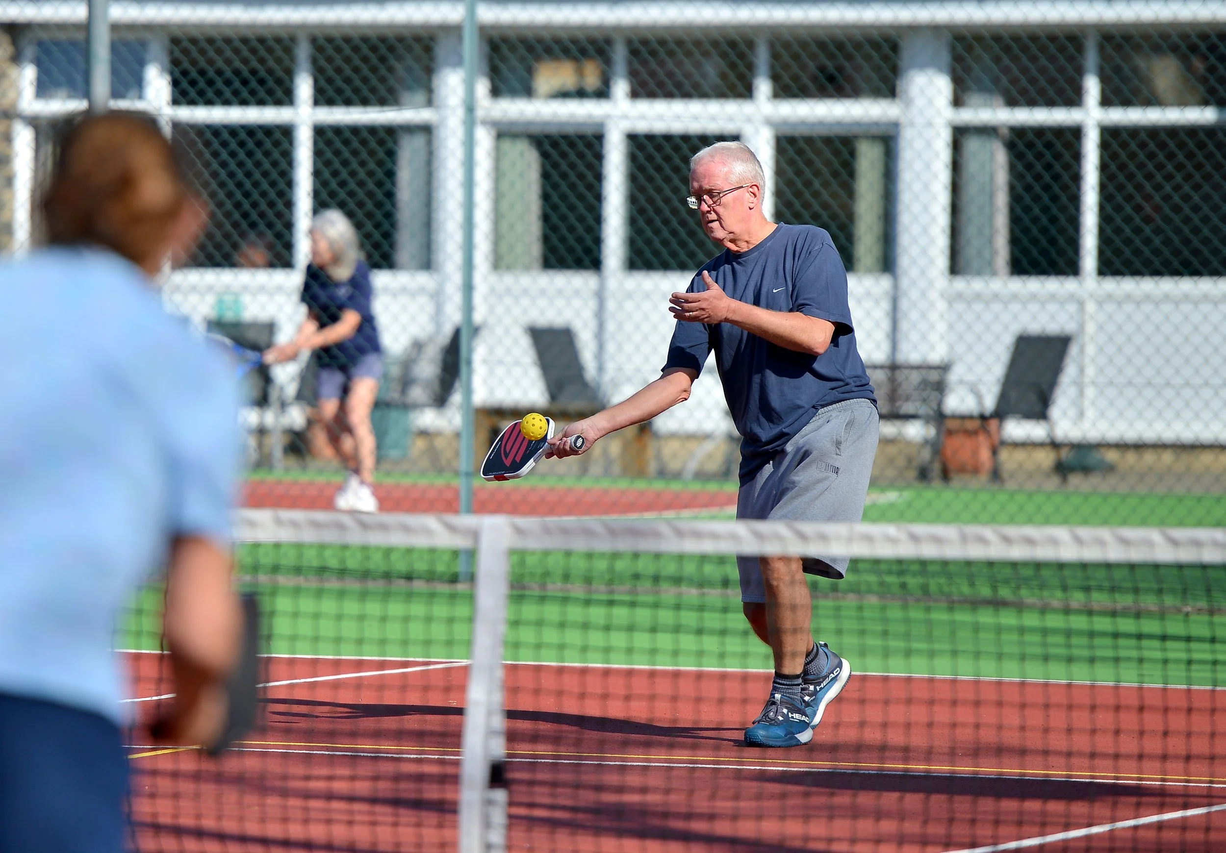 A person playing pickleball on an outdoor court during the day, holding a paddle and hitting a yellow ball.