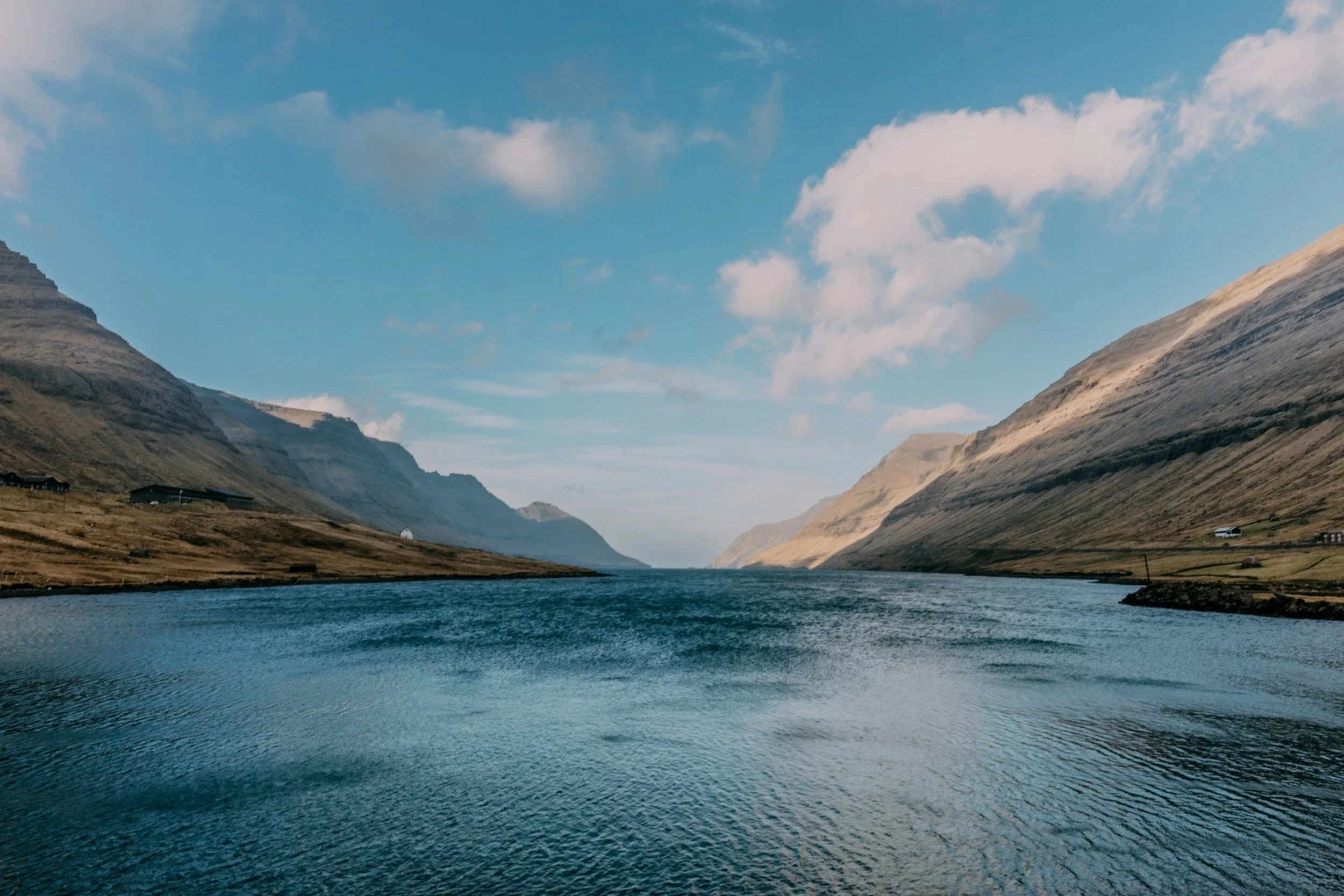 A wide river flowing through a valley with mountains on both sides, under a partly cloudy sky.