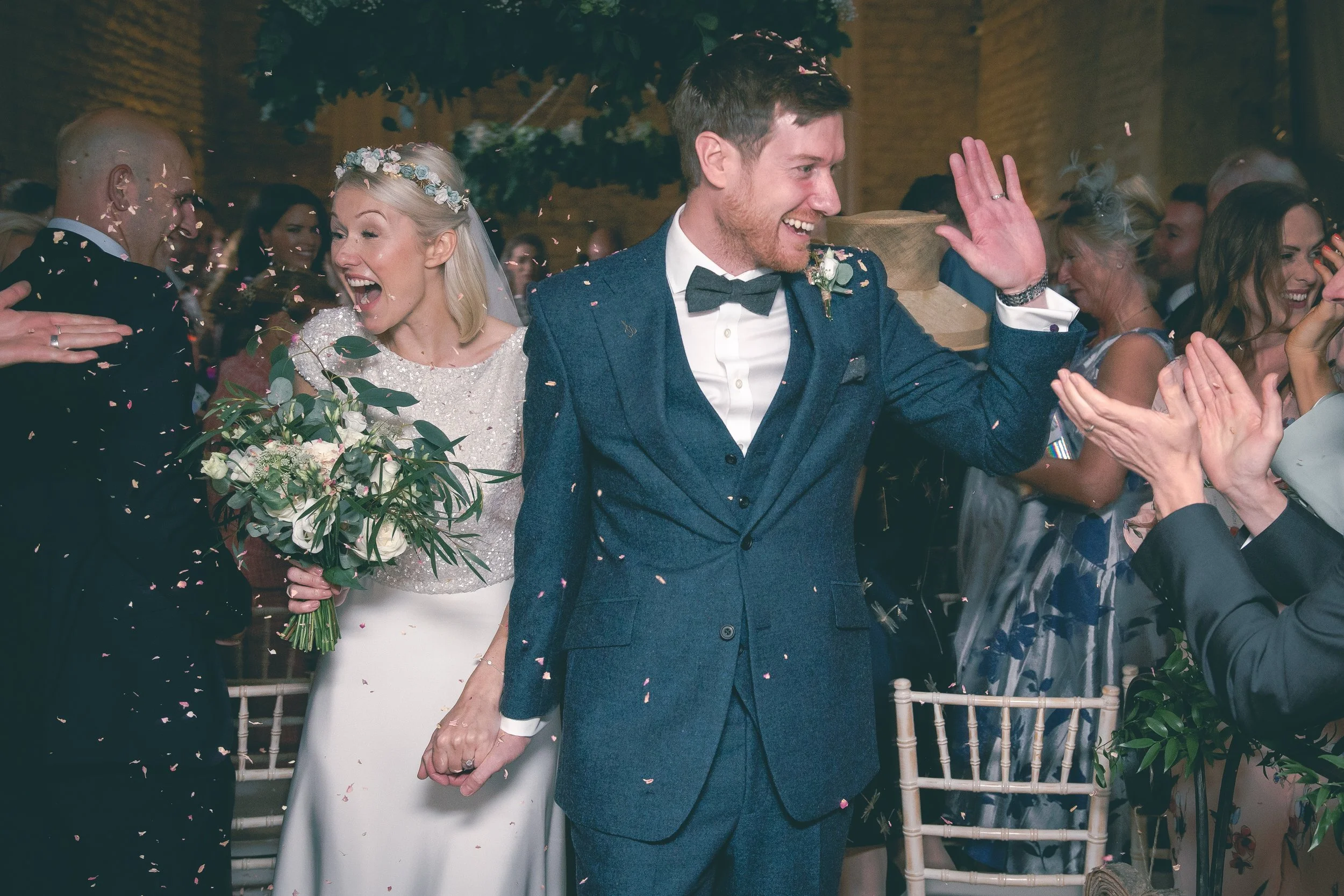 A newly married couple walking hand in hand at their wedding reception, surrounded by happy guests, confetti falling in the air, and joyful expressions.