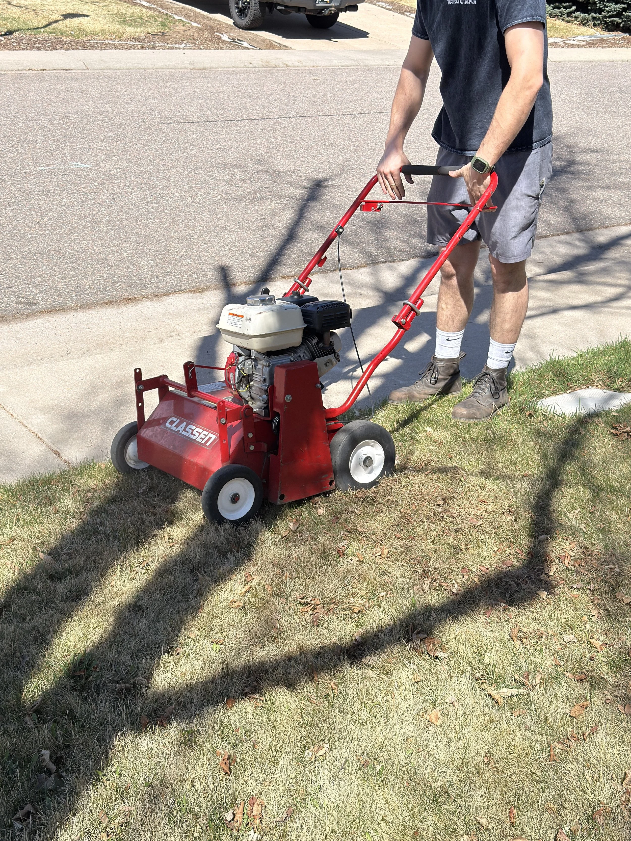A gas-powered mechanical power rake being used by Big Sam Sprinklers for a spring lawn cleanup in Littleton. Professional dethatching equipment designed to aggressively lift matted grass and reset residential turf.