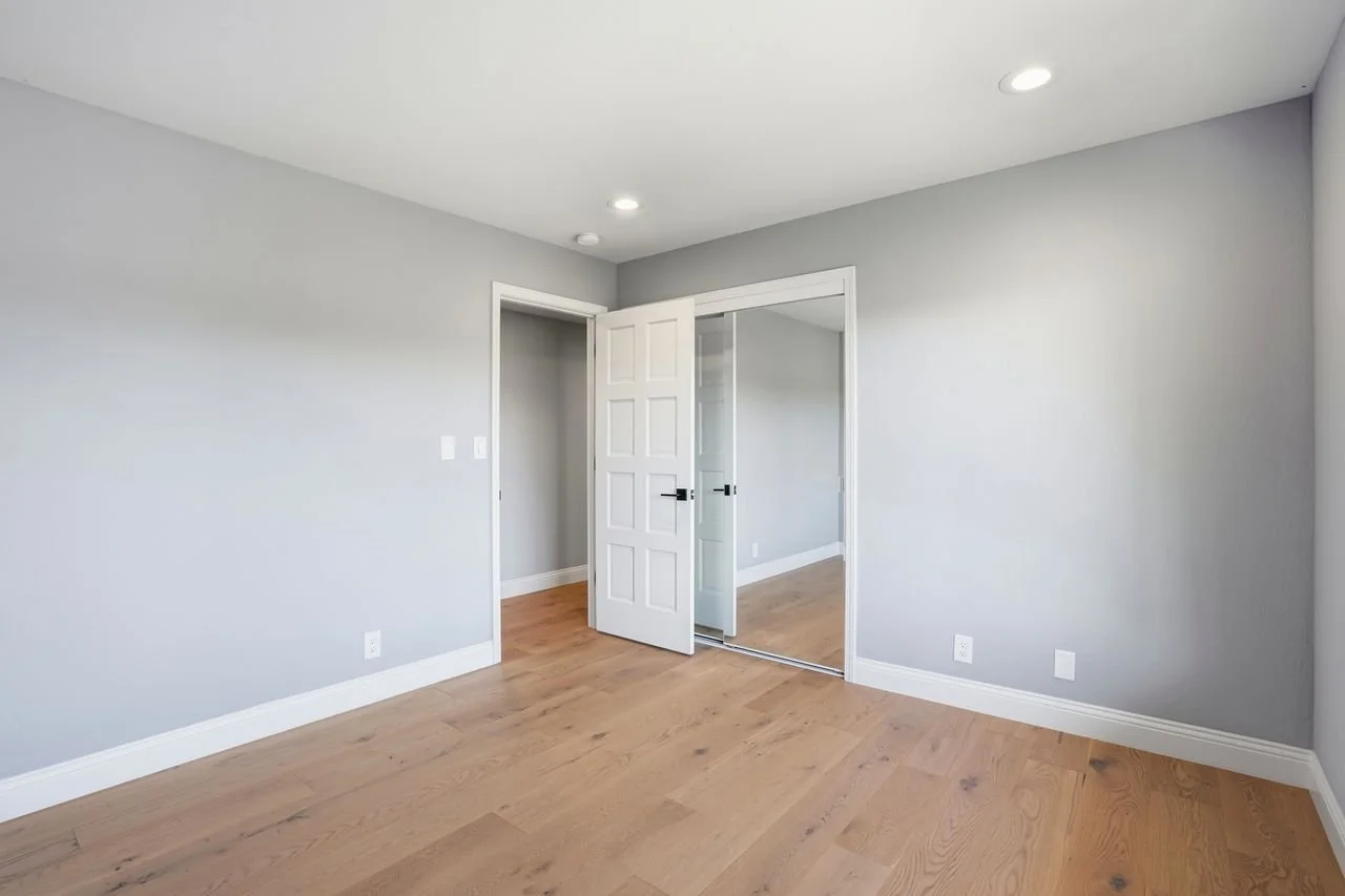 Empty room with gray walls, hardwood floor, and a door with a mirror sliding closet.
