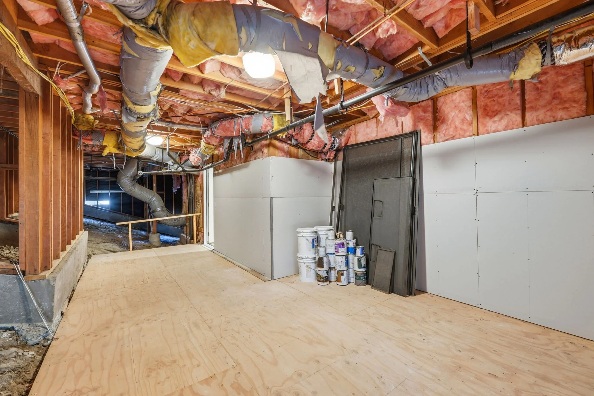Construction site with exposed ceiling and insulation, pipes, drywall, and construction materials like paint cans and panels.
