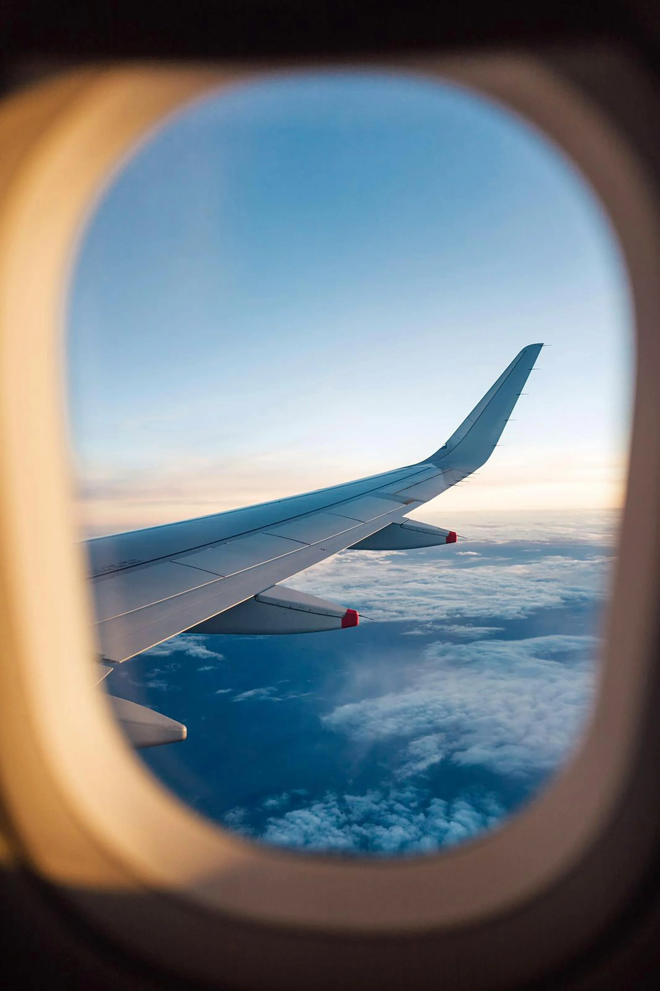 Vista desde la ventanilla de un avión, mostrando la ala del avión y nubes en el cielo al atardecer.
