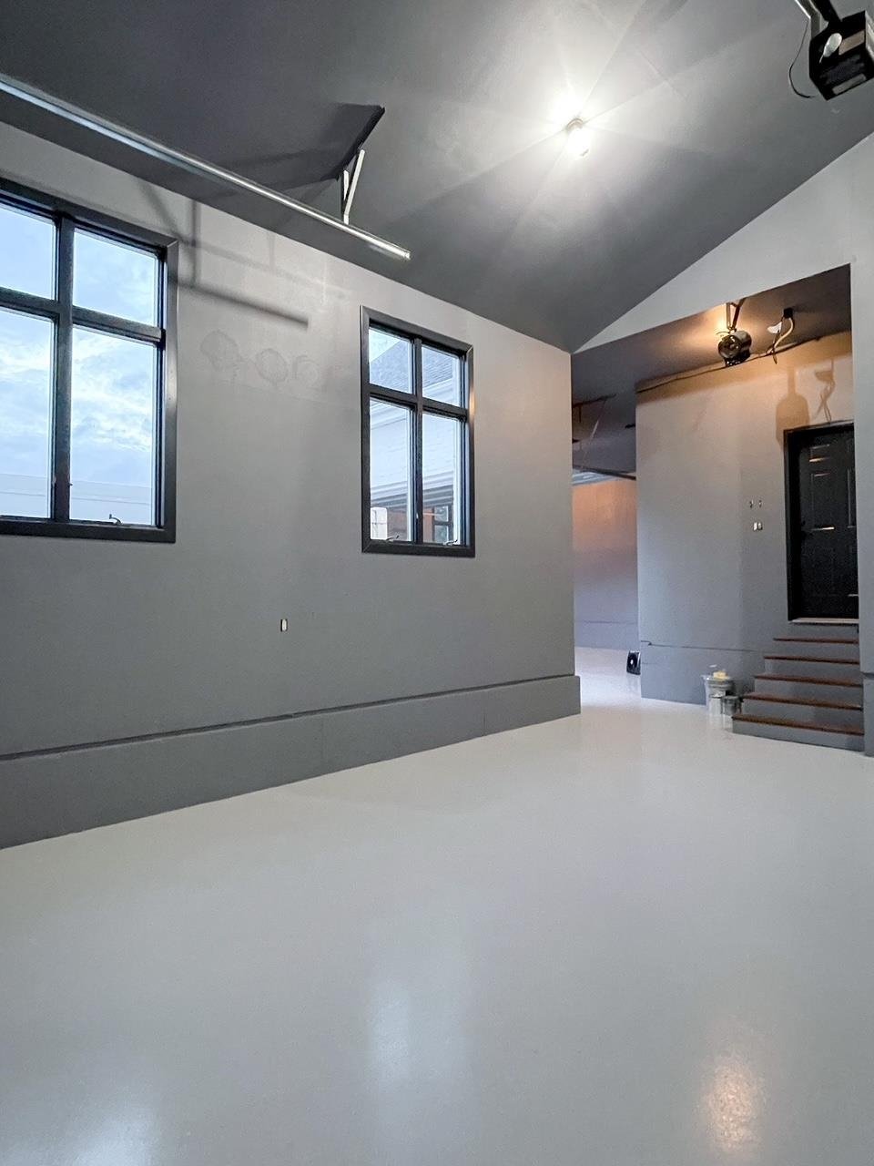 Empty room with gray walls, black framed windows, ceiling-mounted light fixtures, and a staircase leading to a black door.