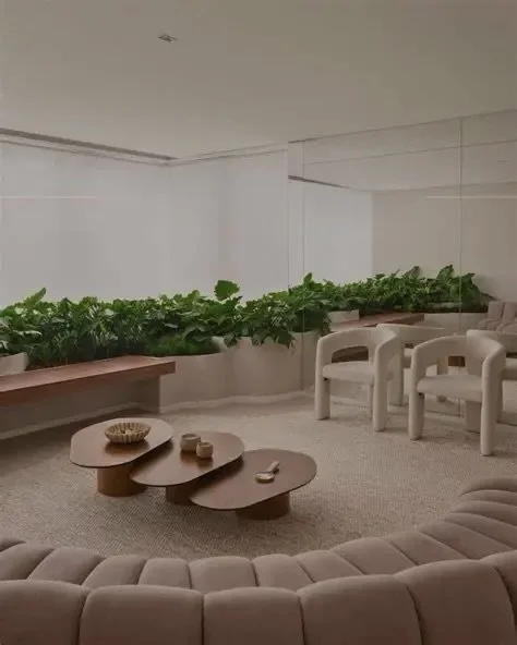 Sala de estar minimalista com poltronas brancas, mesa de centro de madeira e uma fila de plantas verdes na parte de trás ao lado da parede branca.