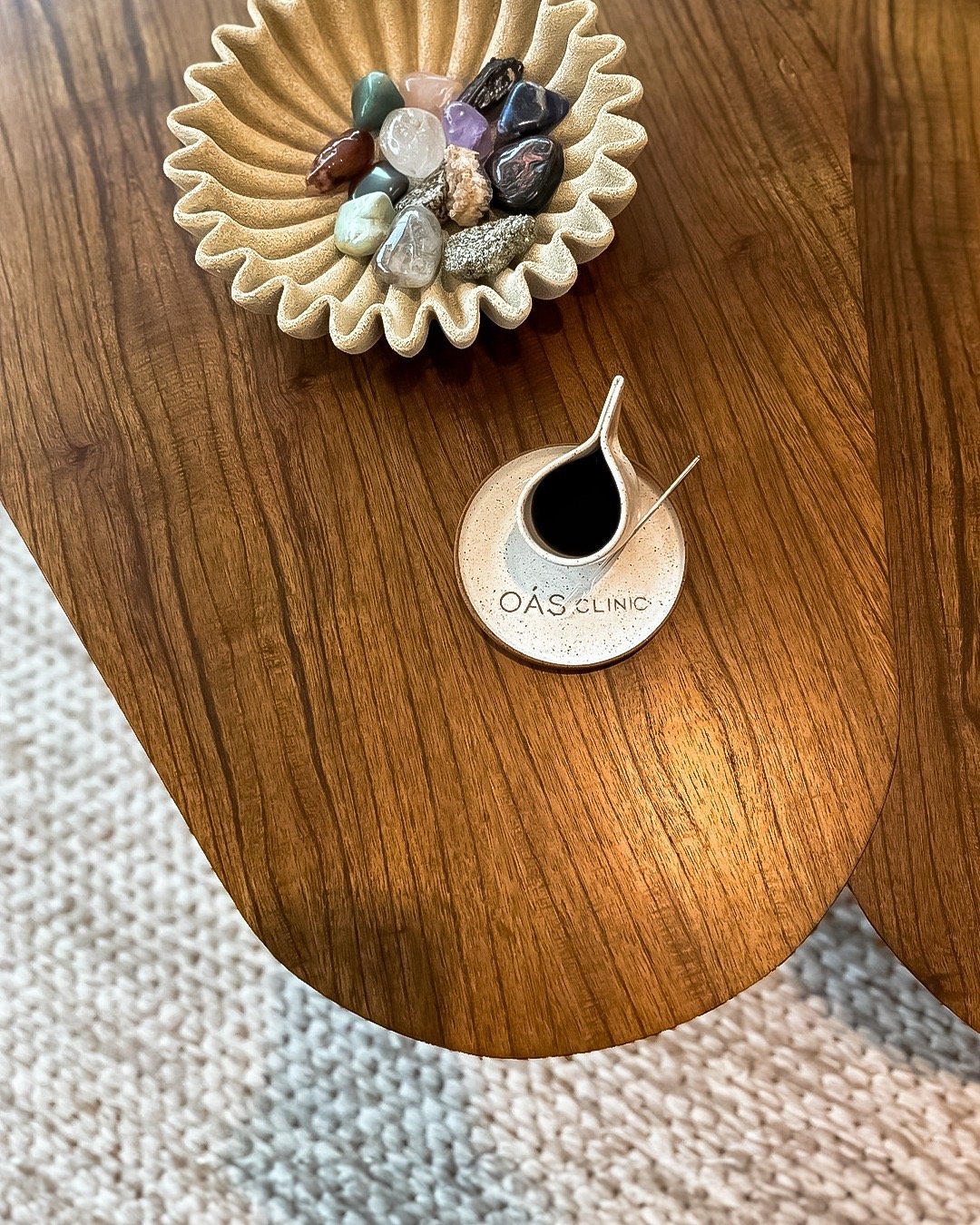 Vaso com líquido escuro sobre mesa de madeira junto de recipiente com pedras decorativas.