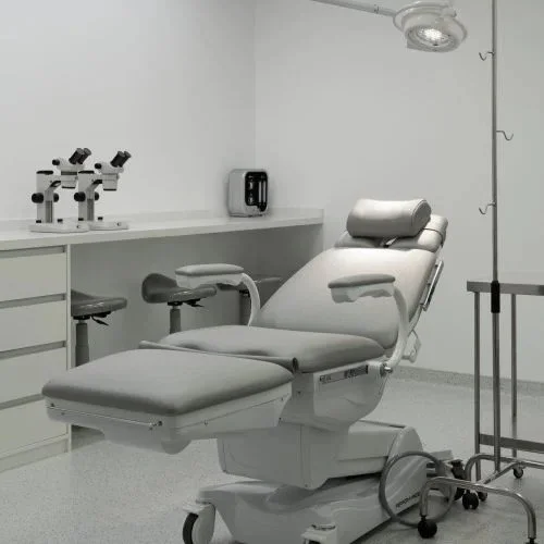 Sala de exame médica com cadeira ginecológica, microscópios e equipamentos médicos.