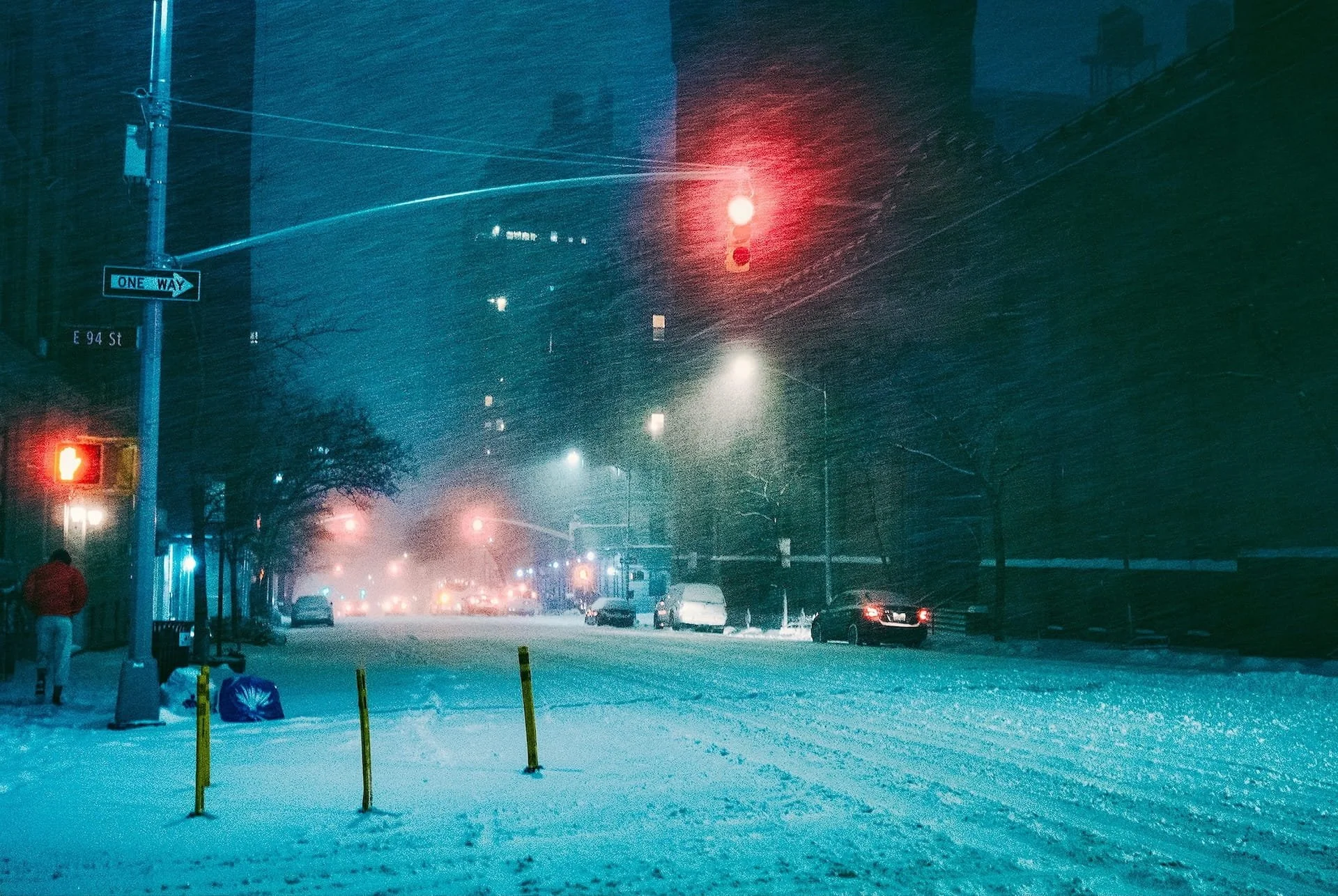 Snow-covered NYC street at night with red traffic lights at E 94th Street intersection