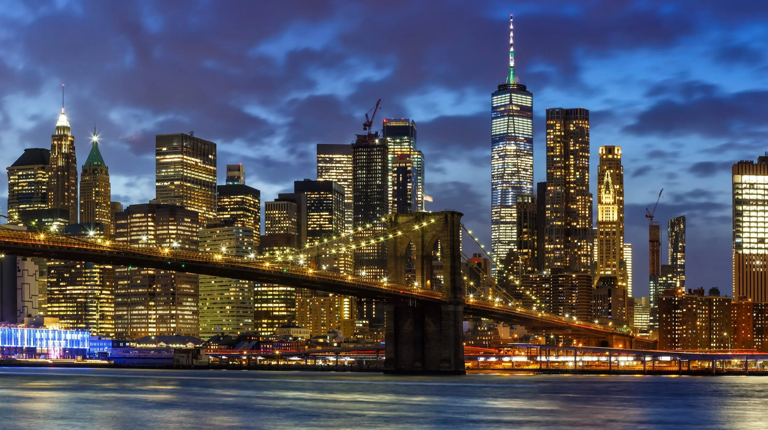 Brooklyn Bridge and Lower Manhattan skyline lit up at night over the East River