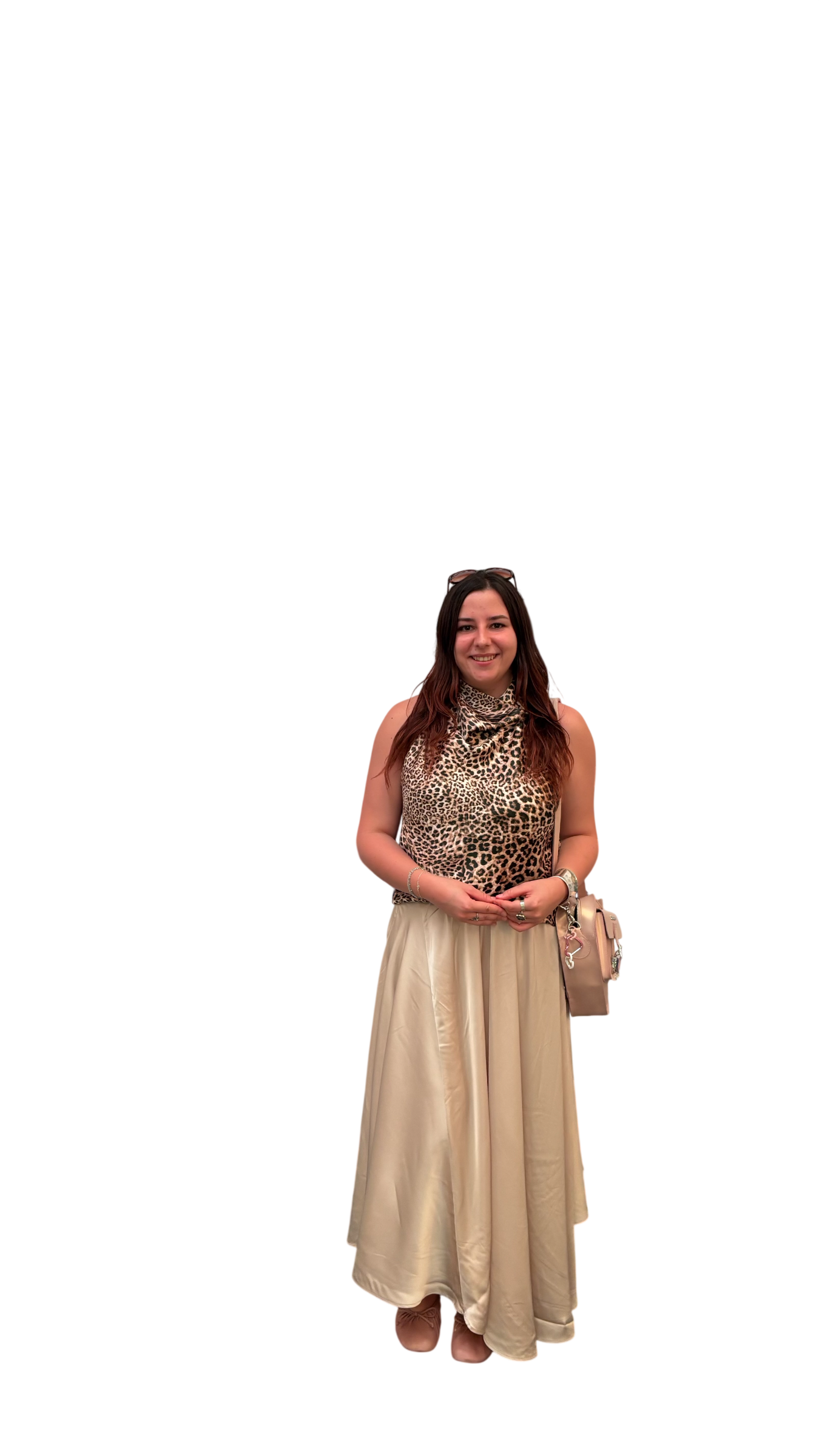 Andreea Popescu, woman standing and smiling, wearing a sleeveless leopard print top, a long beige skirt, and accessories including bracelets, rings, a watch, and sunglasses on her head. She is holding her hands in front and carrying a beige handbag.