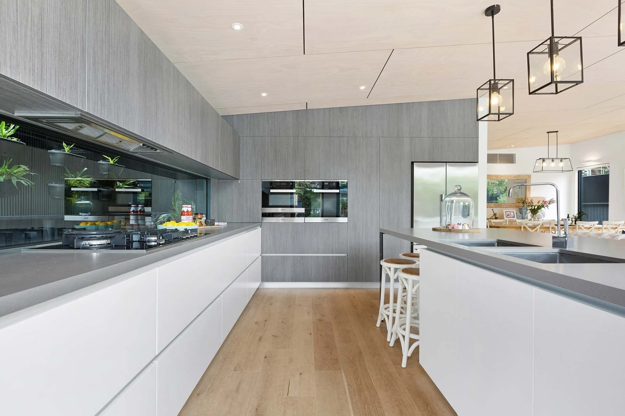 Modern kitchen with white cabinets, gray countertops, wooden floor, and contemporary lighting fixtures.