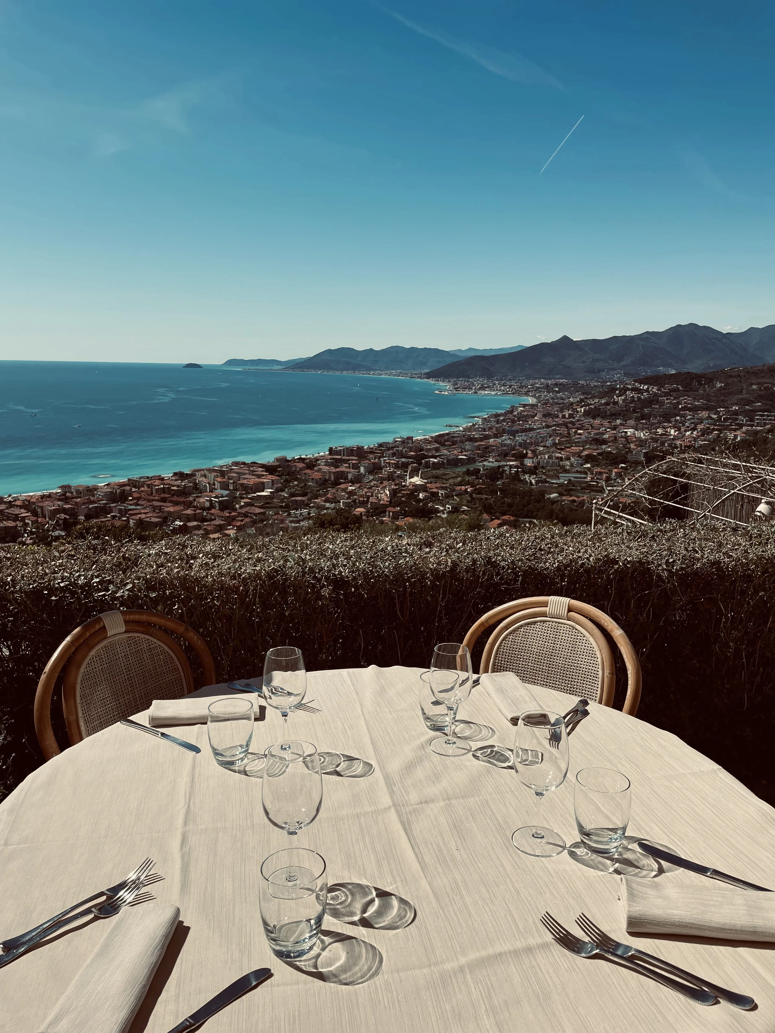 Tavolo imbandito con bicchieri e posate, vista panoramica sul mare e sulle montagne