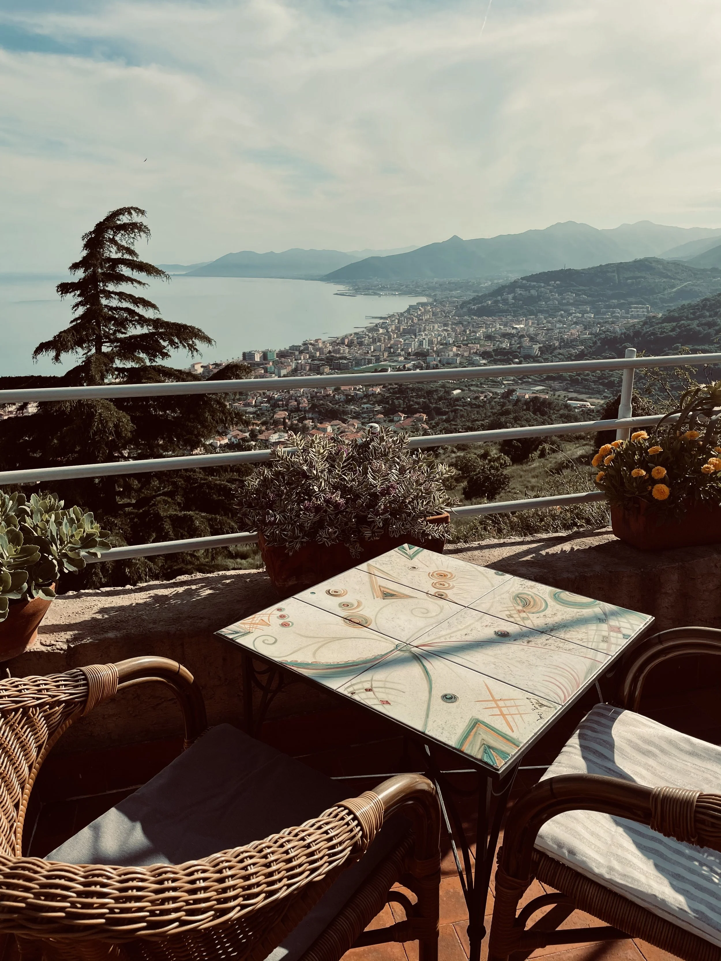 Vista panoramica di un mare e di una città, vista da un terrazzo con tavolo e sedie di vimini e piante ornamentali