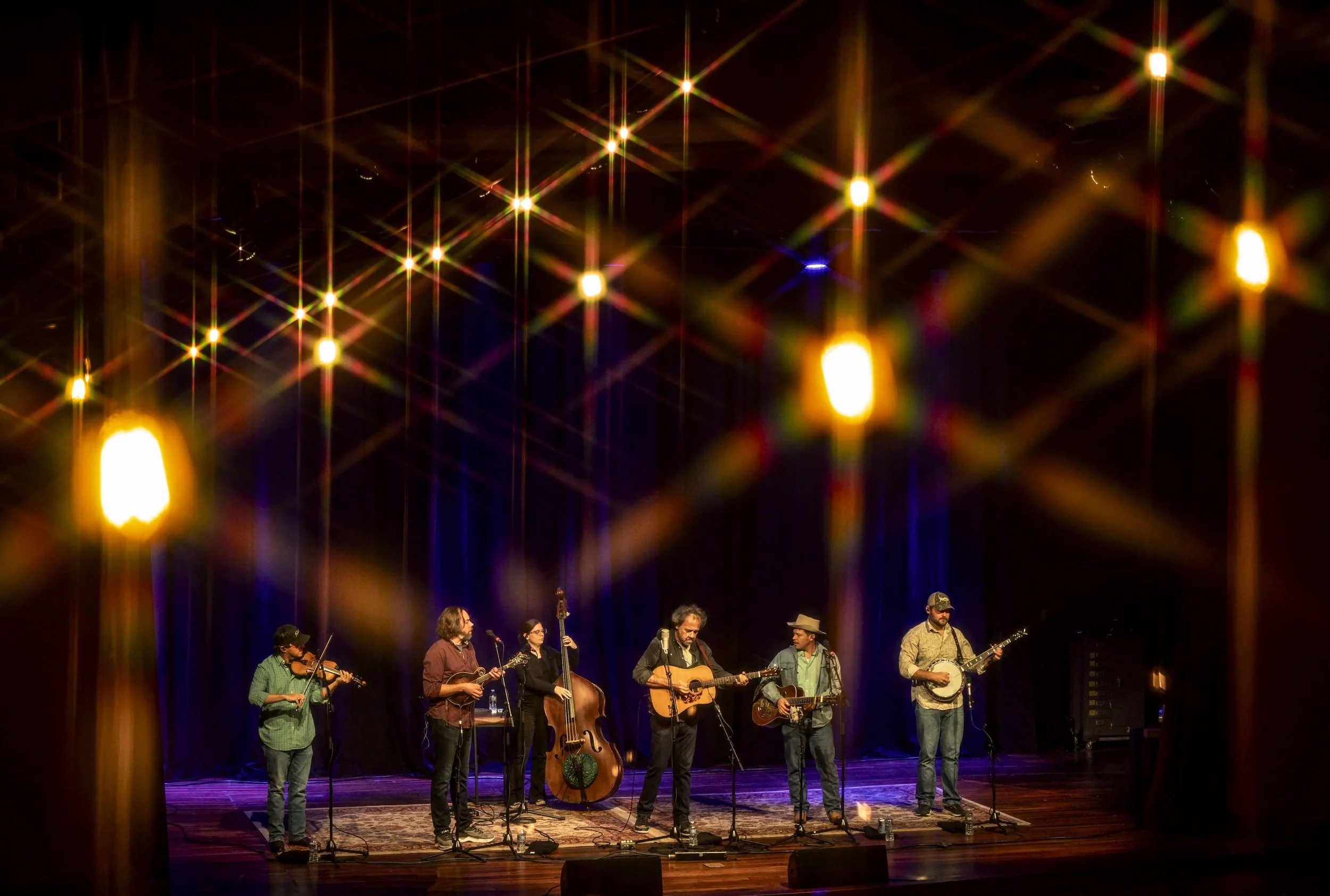 Musicians performing on stage at a concert, illuminated by colorful stage lights.