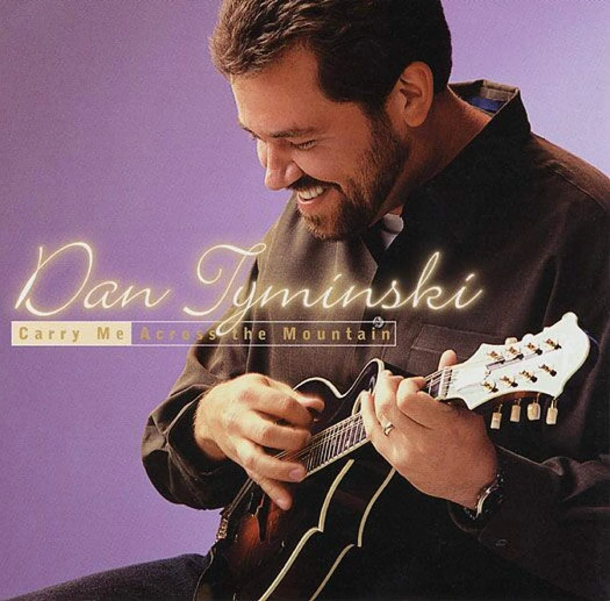 Album cover featuring Dan Tuniski smiling while playing an acoustic guitar against a purple background, with the title "Carry Me Across the Mountain" in stylized text.
