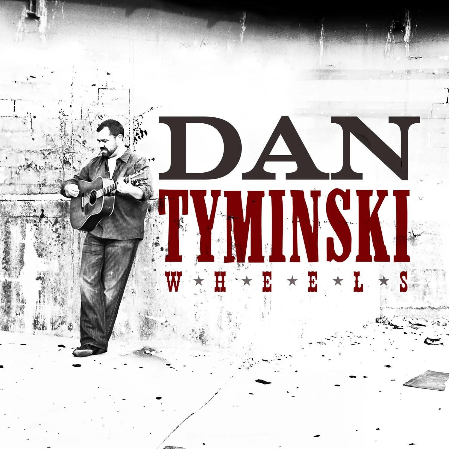 Black and white photo of a man playing guitar against a weathered wall, with text overlay reading 'DAN TYMSKI WHEELS' in large letters.