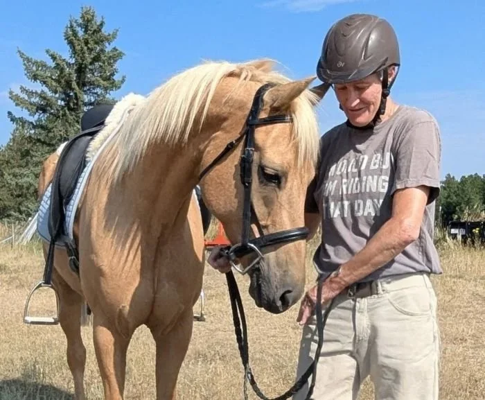 A man in a helmet standing with a blonde horse in an open field, touching its forehead.