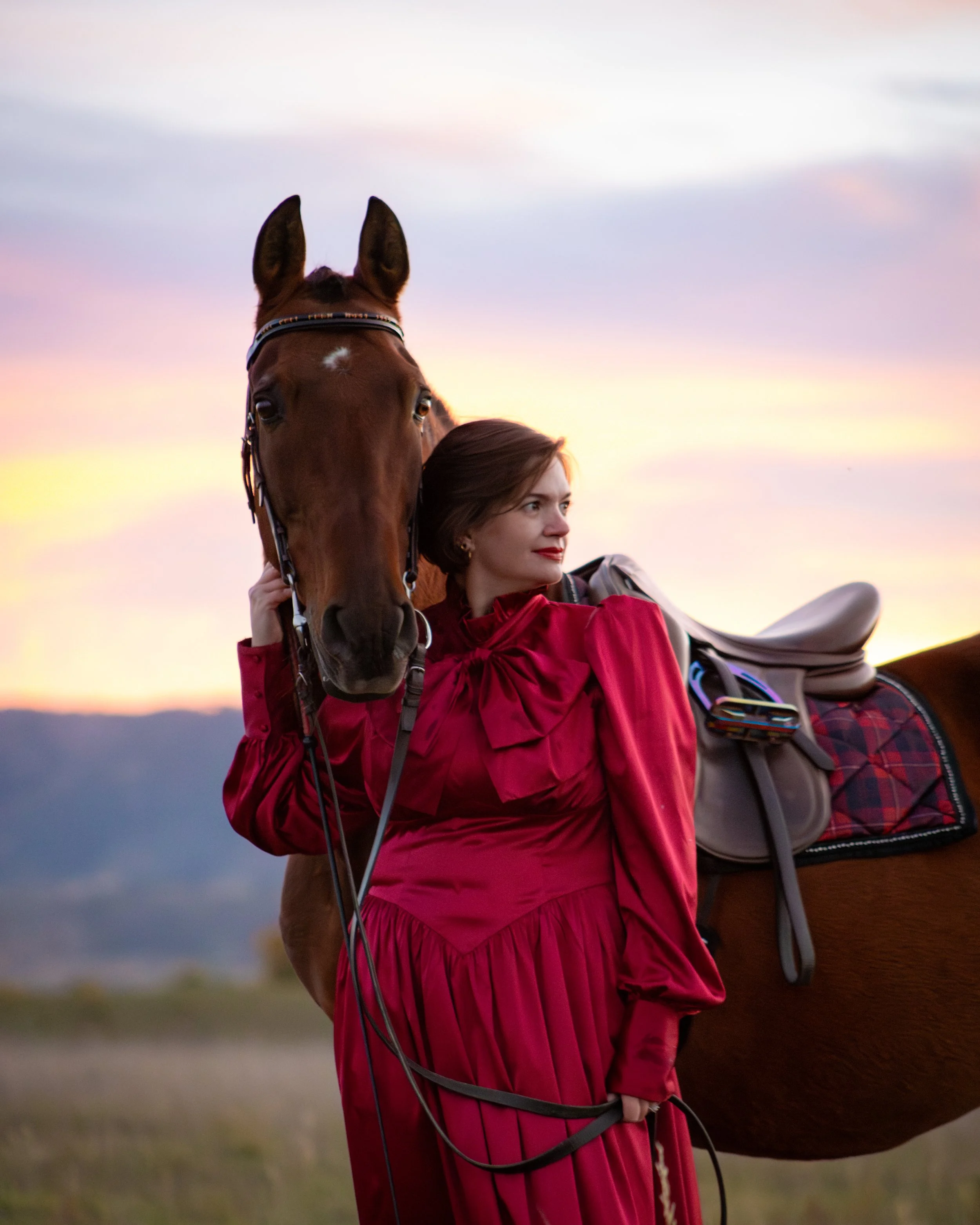 Woman in a red dress standing with a horse during sunset