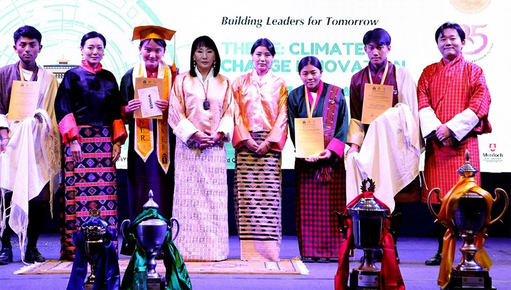 Young students in traditional Bhutanese attire standing on stage with certificates and trophies, participating in an awards ceremony focused on climate change and innovation.