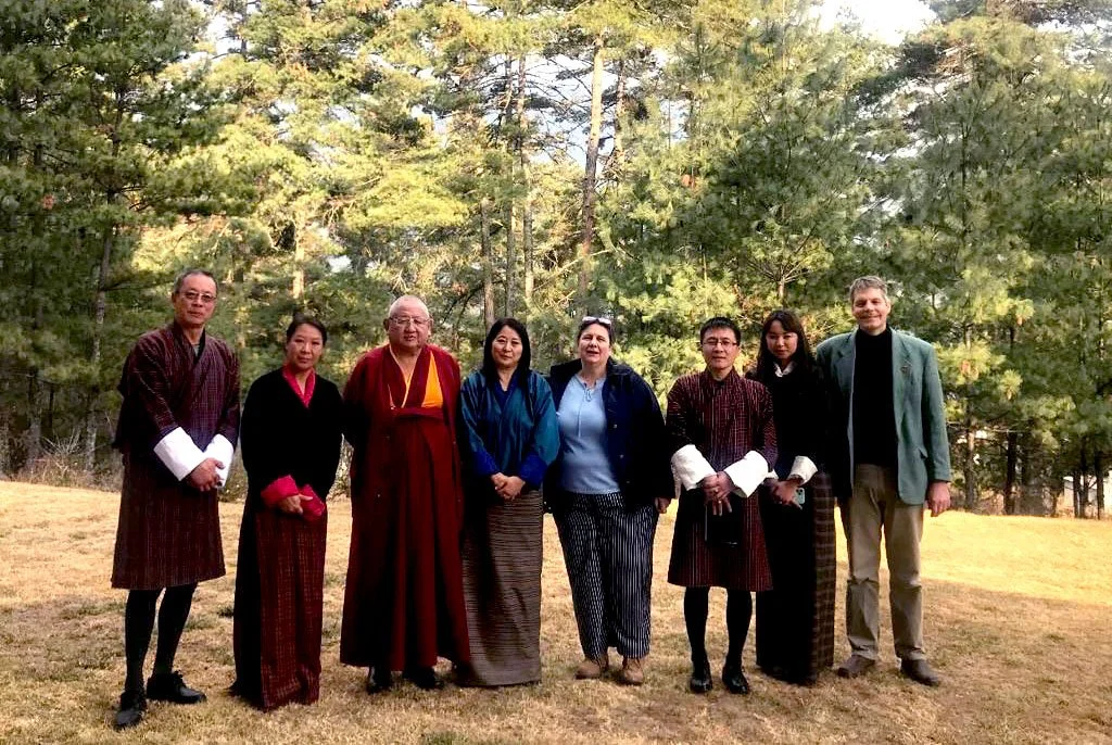Group of eight people standing outdoors on grass with trees in the background, dressed in traditional and casual clothing.