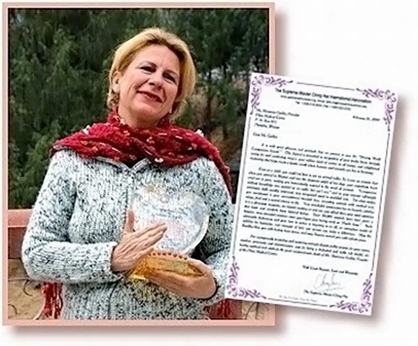 A woman with blonde hair holding a glass trophy or award, standing outdoors with trees in the background. Next to her is a framed document or certificate with purple decorative borders and text.