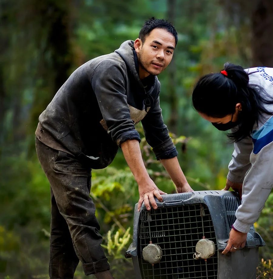 Two people handling a pet carrier in a forest setting