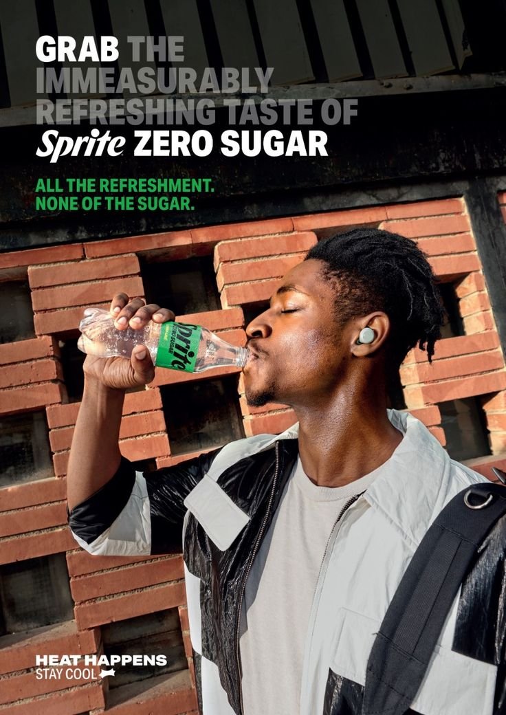 A young man with short dreadlocks drinking Sprite Zero Sugar from a plastic bottle outdoors against a brick wall. He is wearing a white and black jacket, wireless earbuds, and carrying a backpack.