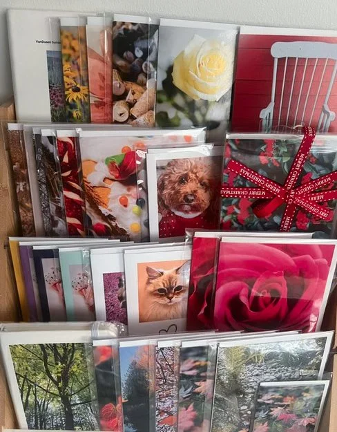 A display stand filled with various greeting cards, including floral designs, animals, and holiday themes, some decorated with ribbons.