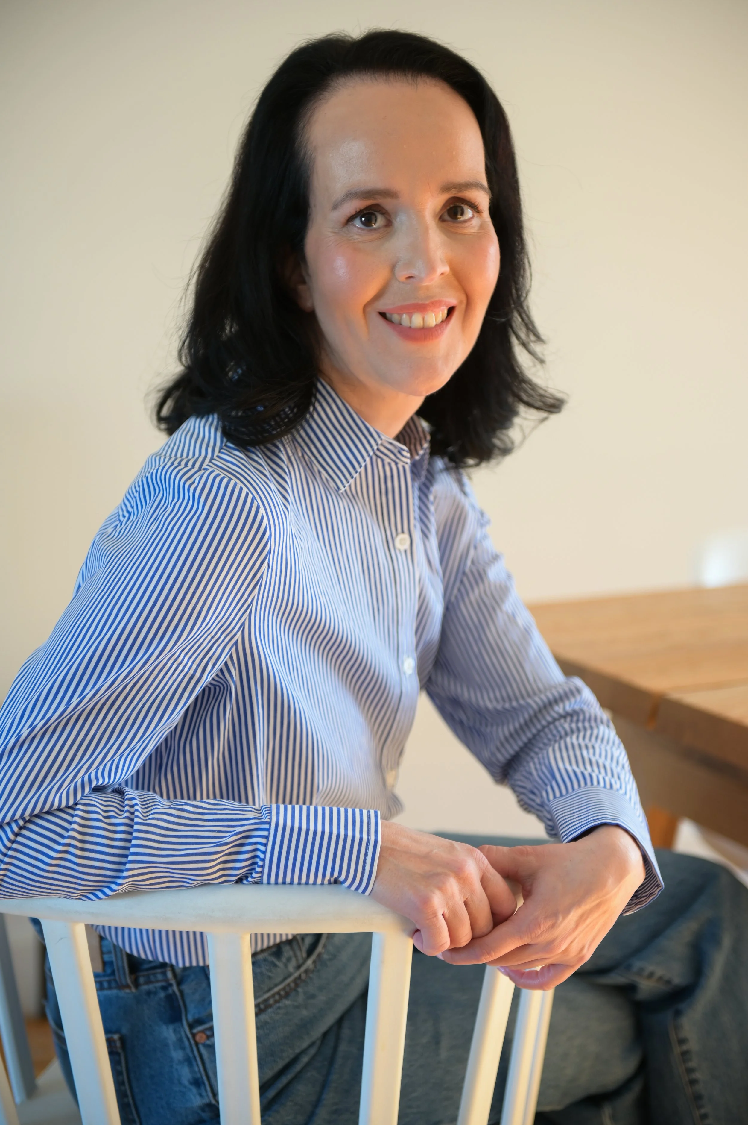 A woman with black hair and a striped blue and white shirt smiling and sitting at a table.
