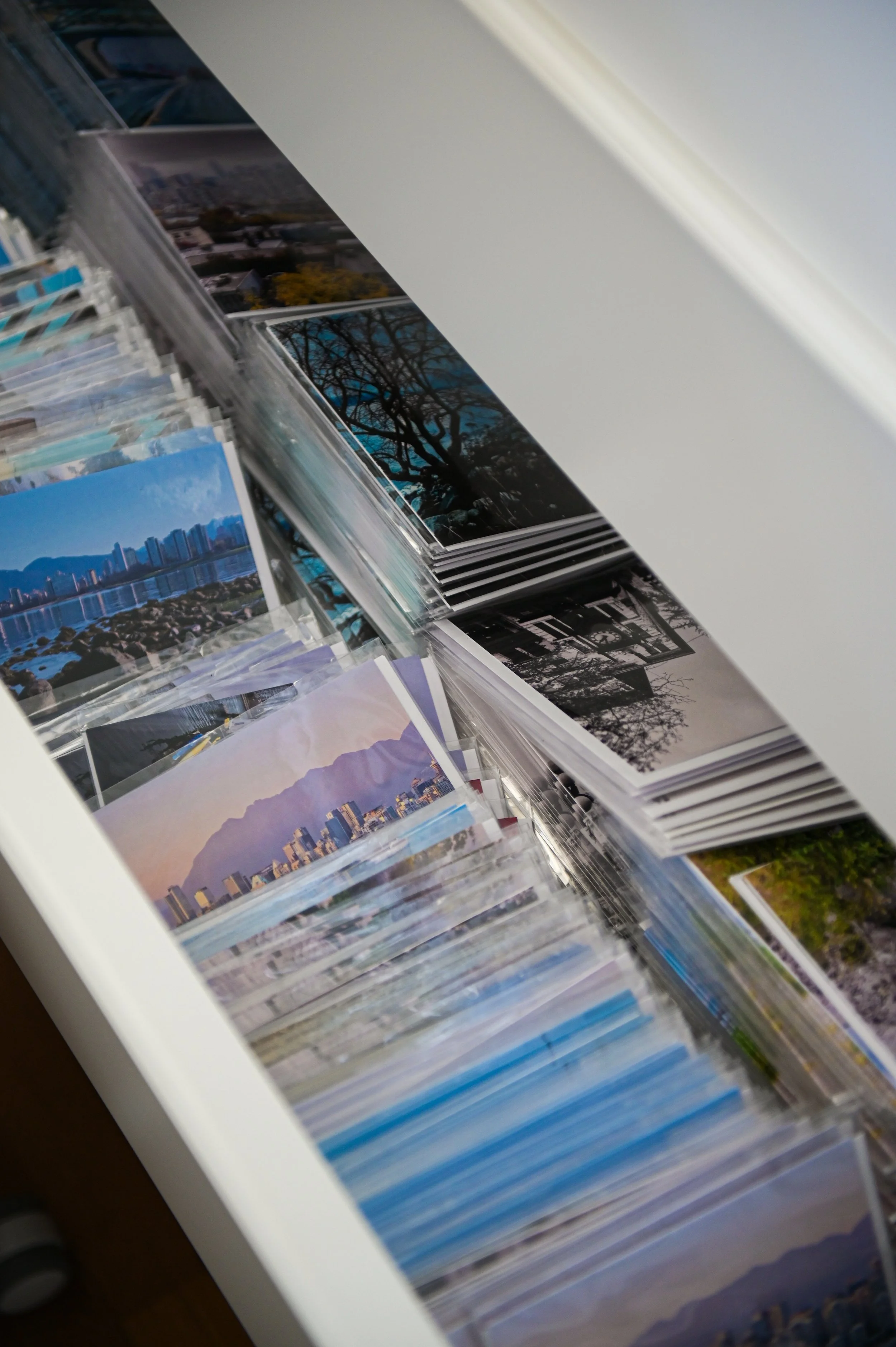 A collection of postcards or photographs arranged in a box, some showing cityscapes, landscapes, and trees with various colors and backgrounds.